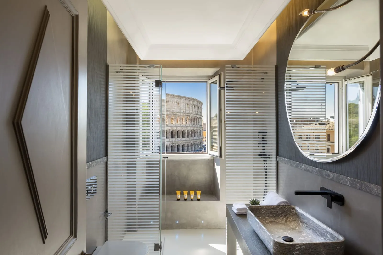 Master Room bathroom at Palazzo Manfredi: a stone basin and a glass shower with a window onto the Colosseum