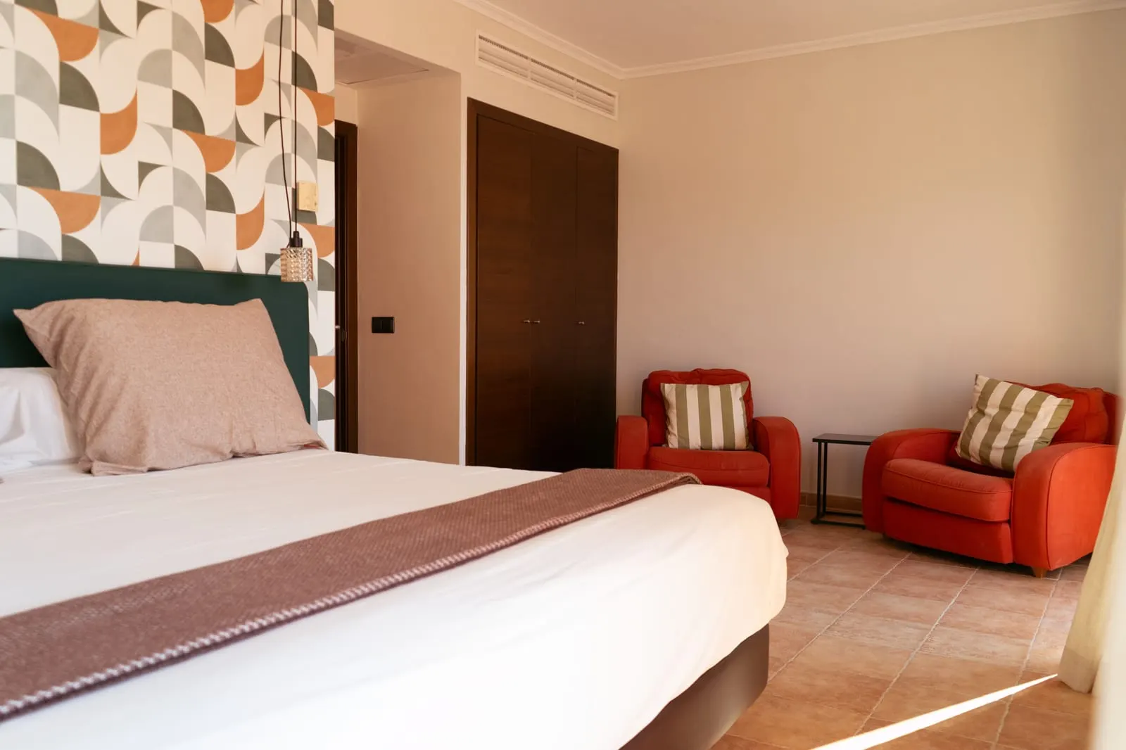 Suite Terrace at Maristel Hotel & Spa: a bed with a green headboard, a fitted wardrobe and two orange armchairs on a terracotta floor