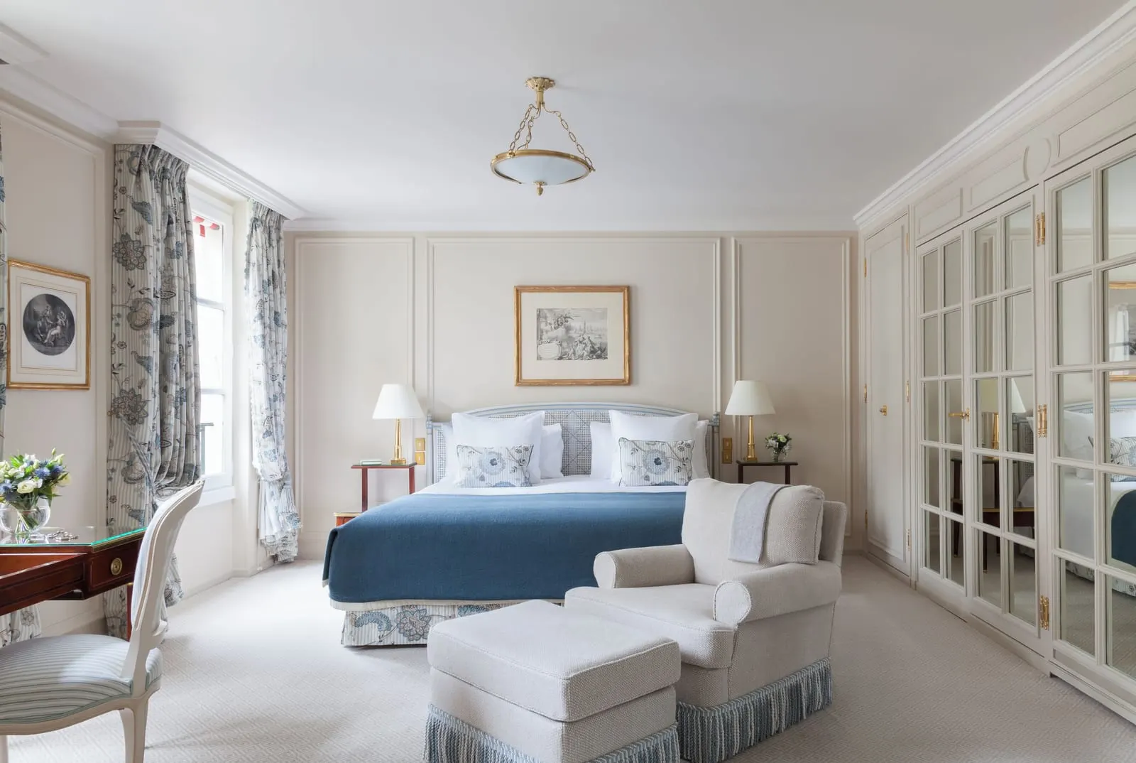 Deluxe Suite Garden at Le Bristol Paris: a bed with a navy throw, an armchair and footstool at its foot, and a wall of mirrored wardrobe doors
