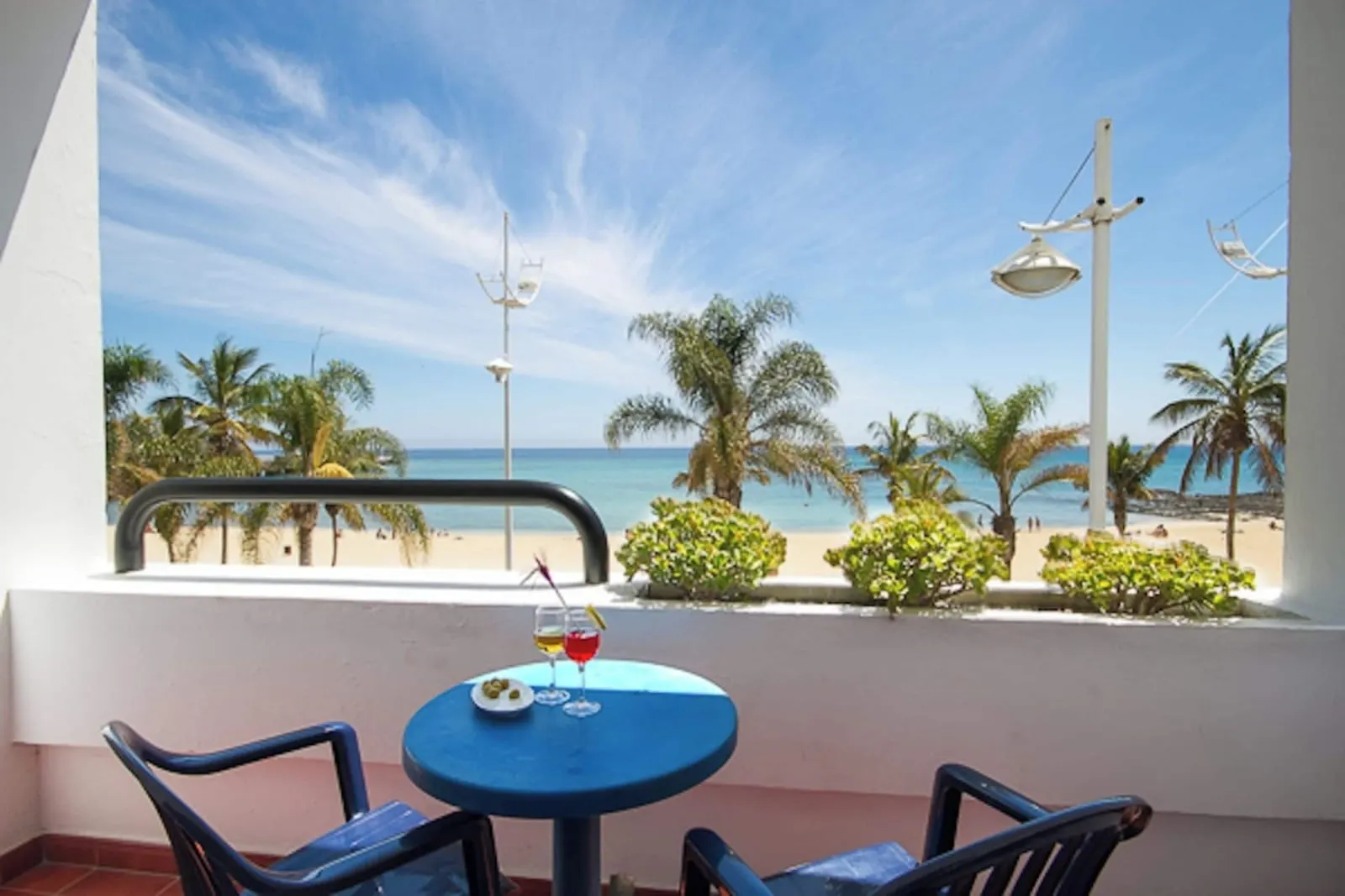 Double Room Sea View at Hotel Lancelot: a balcony with a small round table and a drink, looking over palm trees to the beach and the sea
