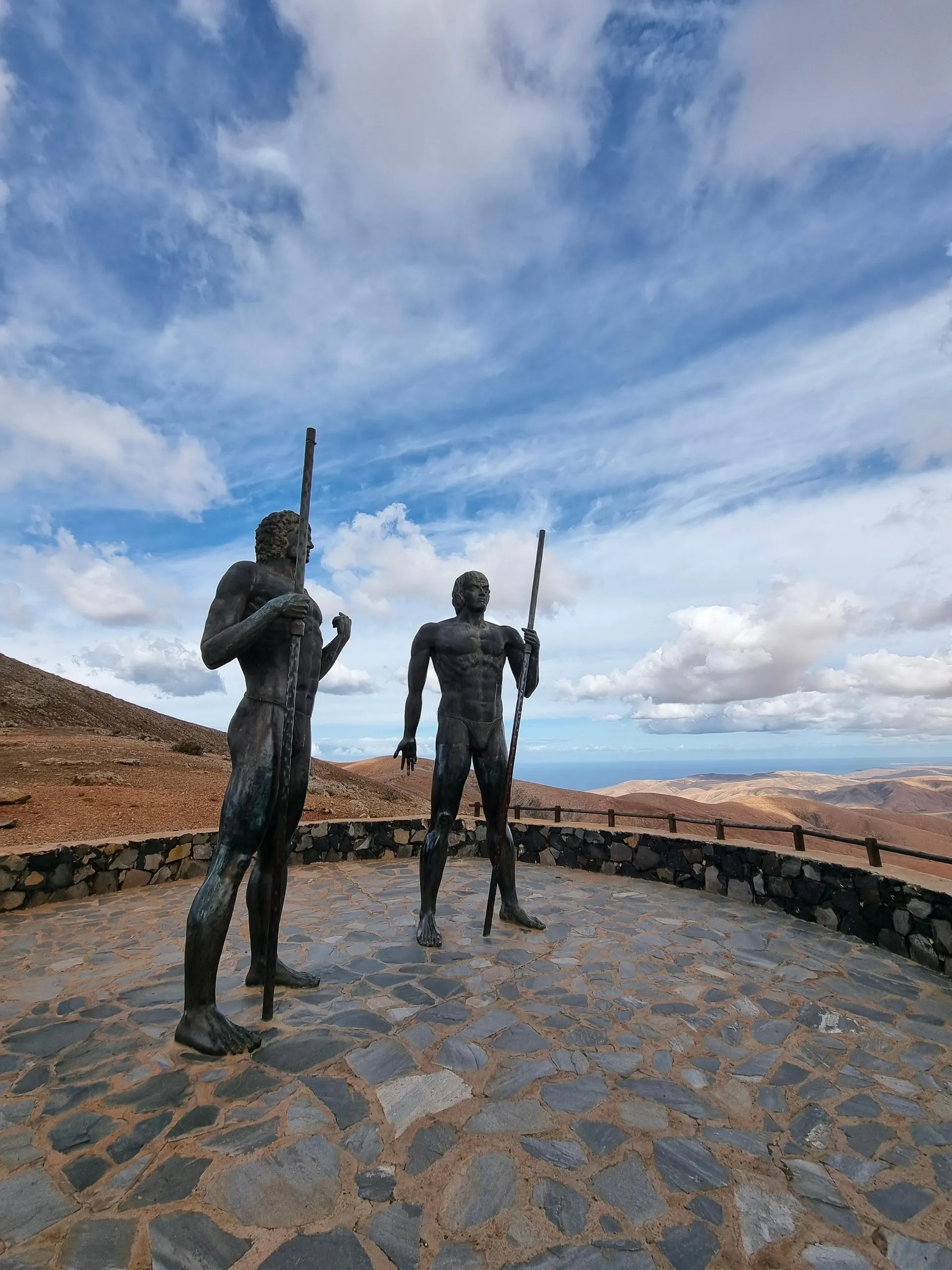 The bronze statues of the aboriginal kings Guise and Ayose on their stone-paved viewpoint, with the hills of the interior behind