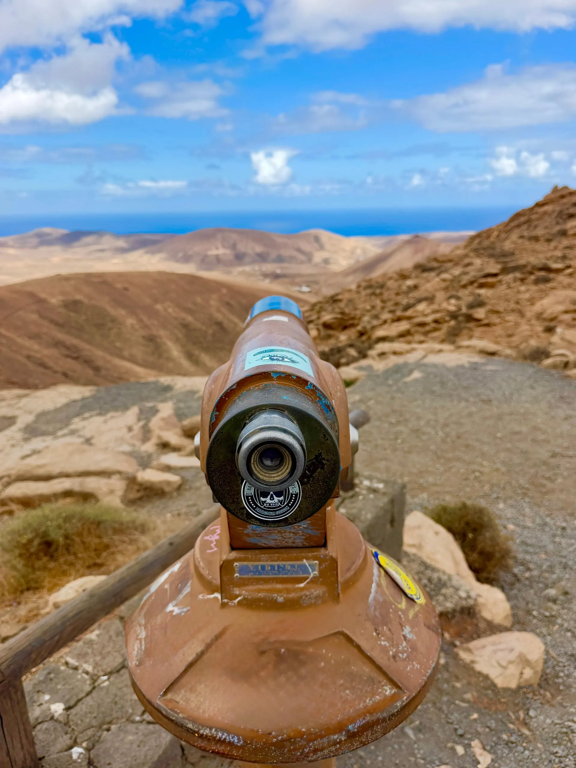 A coin-operated viewing telescope at a mountain viewpoint looking out over brown hills to the sea