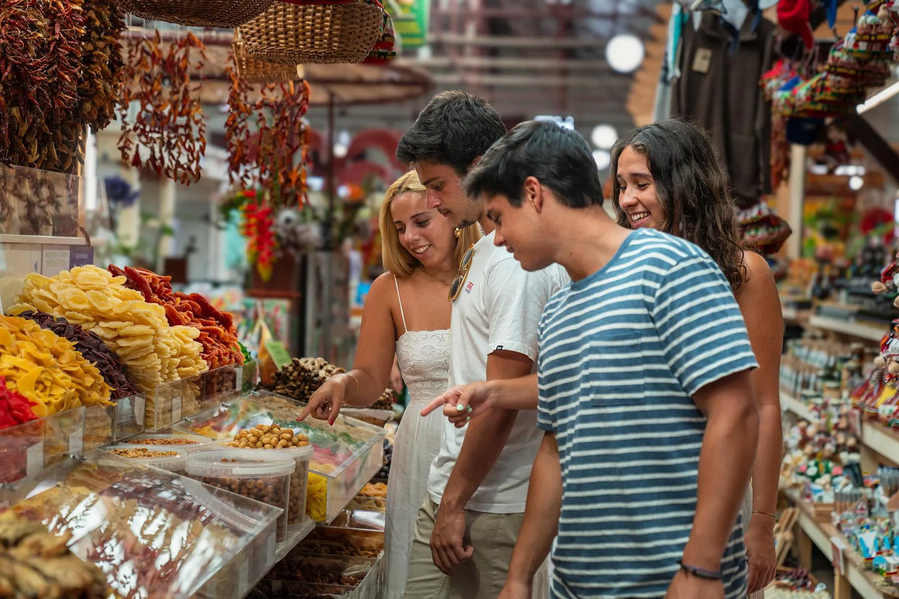 Four young people pointing at dried fruit, nuts and strings of red chillies on a stall in Funchal's farmers' market