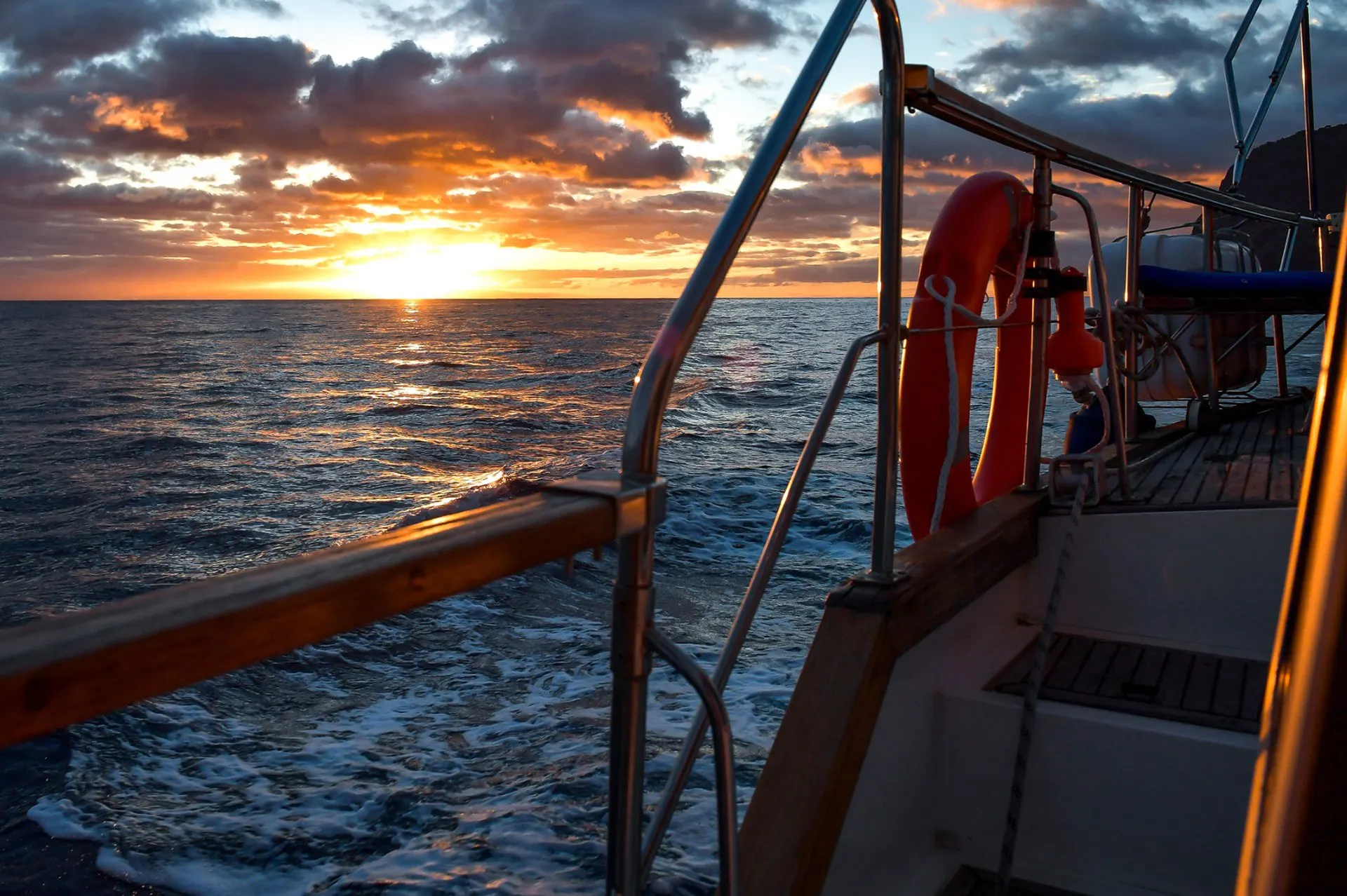 The sun setting over the Atlantic, seen past the rail and lifebuoy at the stern of a yacht