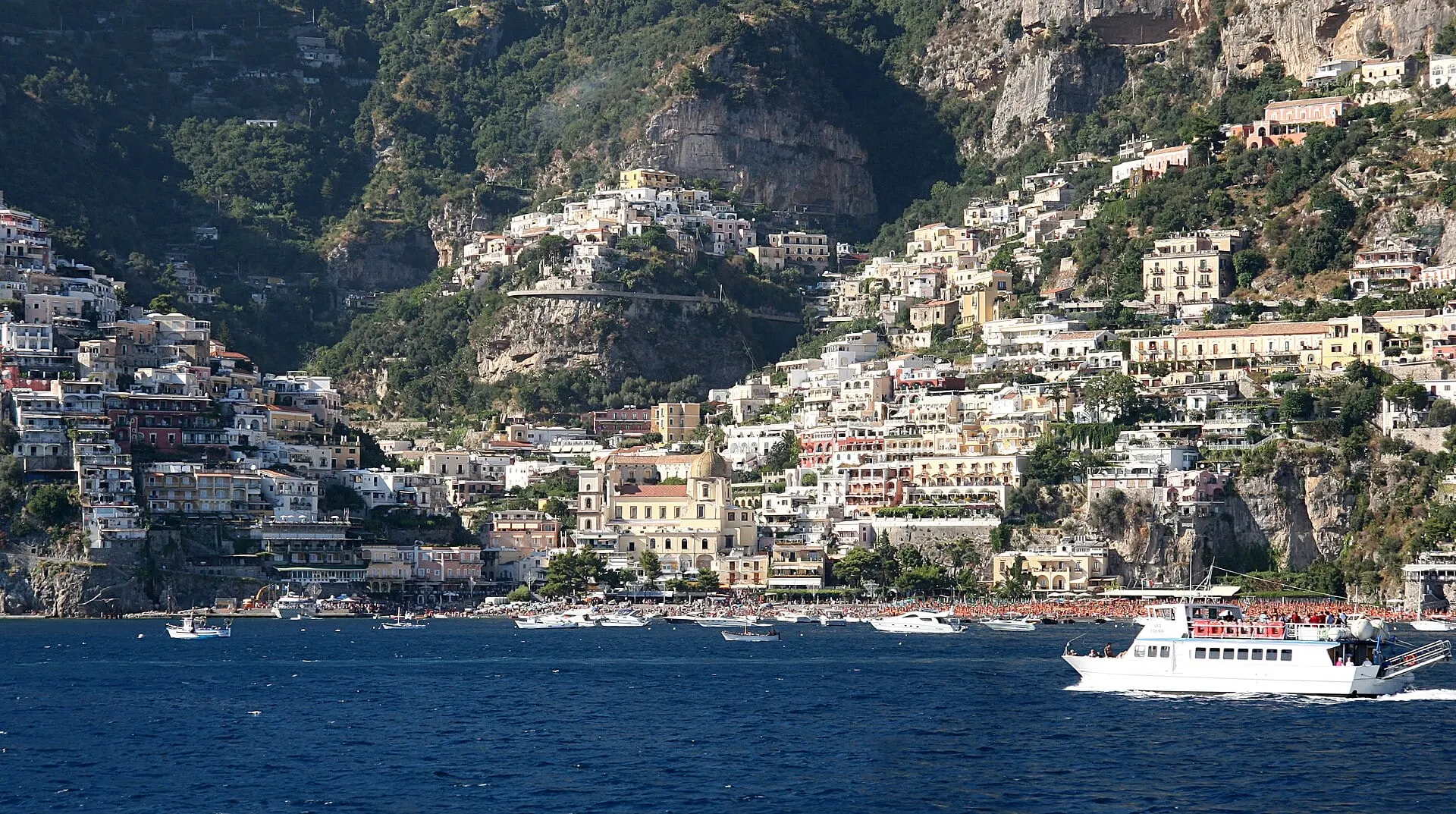 A ferry crossing the deep blue water in front of Positano, its houses stacked up the mountain above the beach