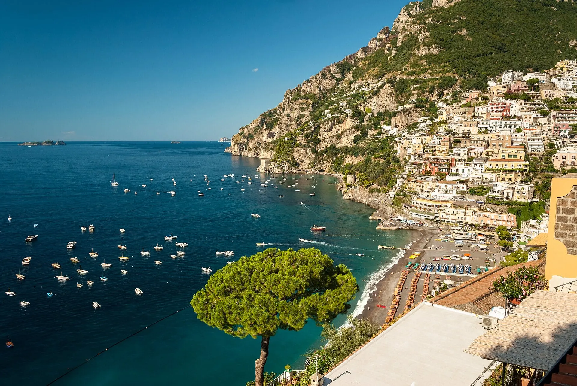 Positano and its beach above a deep blue bay dotted with boats