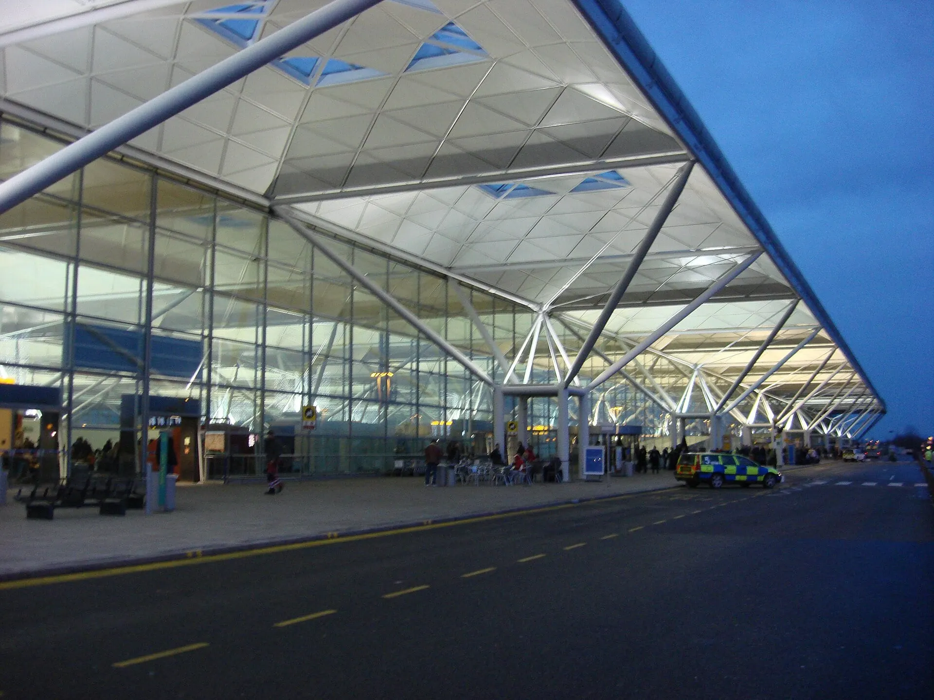The glass front of Stansted Airport terminal at dusk, under its tree-like roof supports