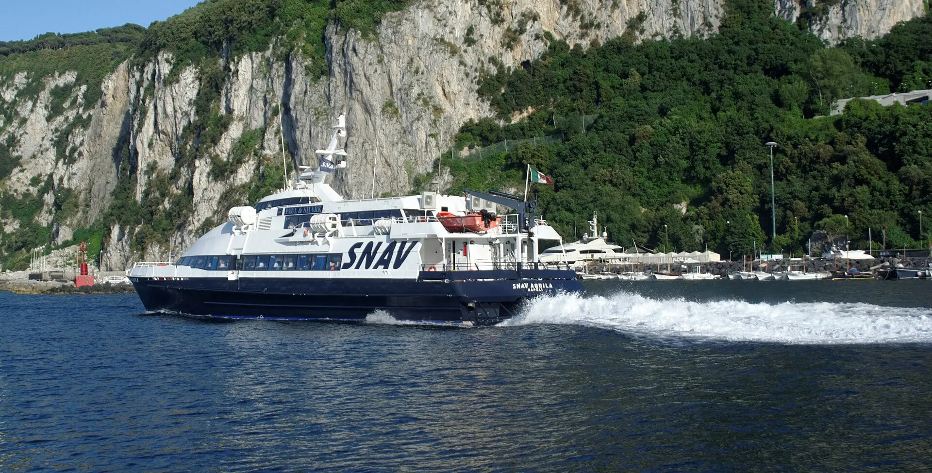 A SNAV hydrofoil speeding out of the harbour at Marina Grande on Capri beneath the island's green cliffs