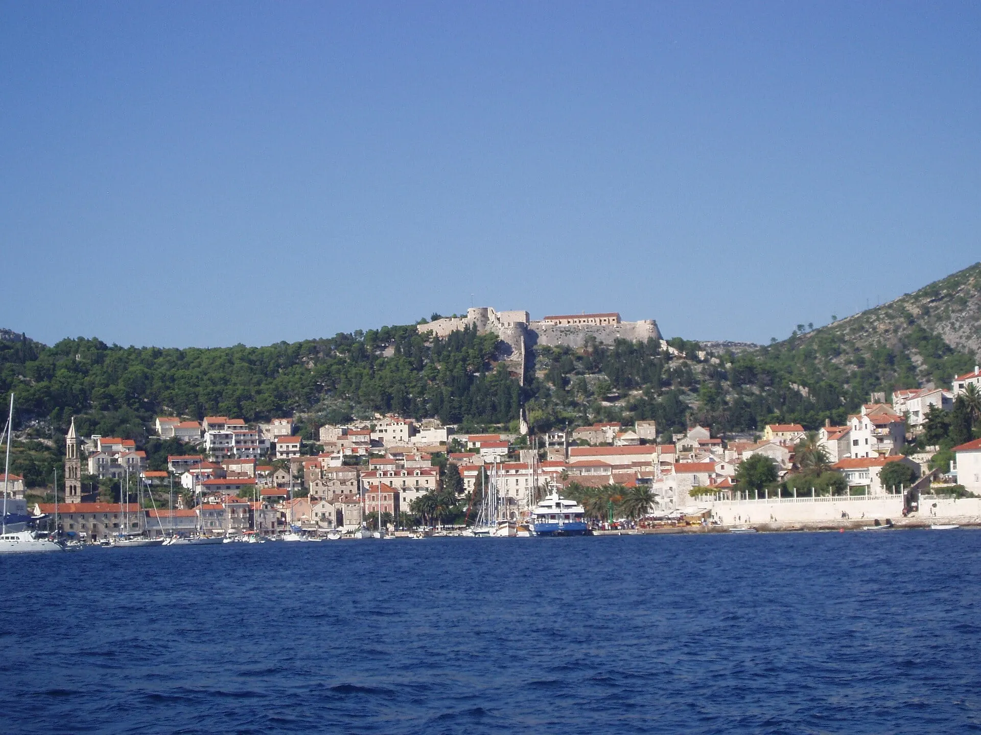 Hvar town on its harbour with the fortress on the wooded hill above, seen from the sea