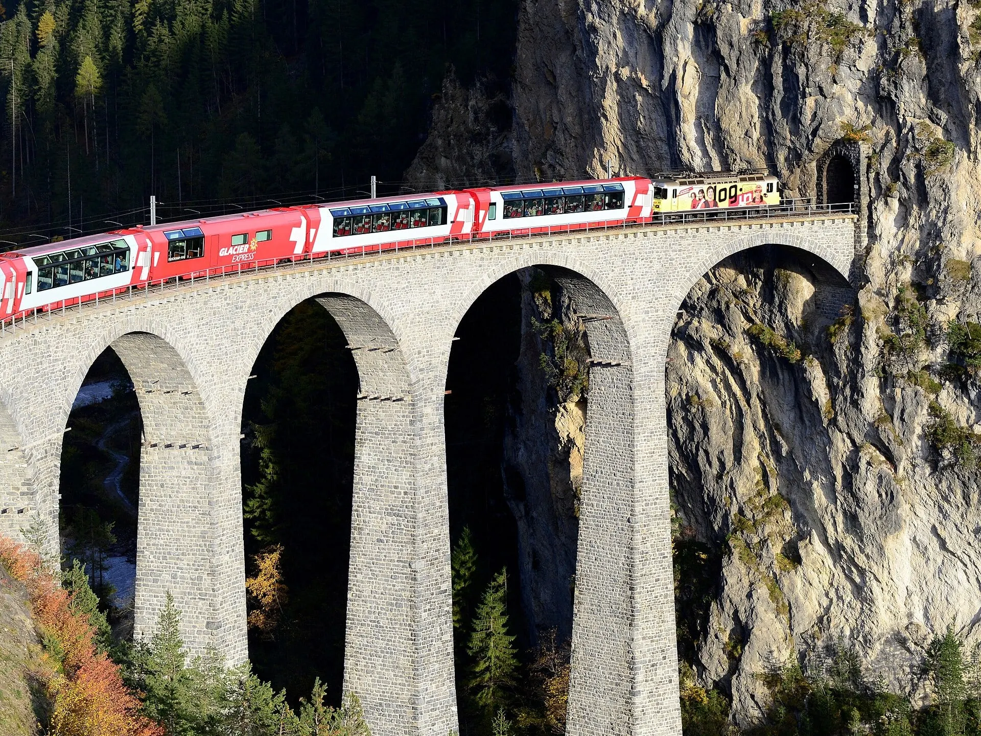 Glacier Express panorama coaches on the stone arches of the Landwasser Viaduct beside the cliff tunnel