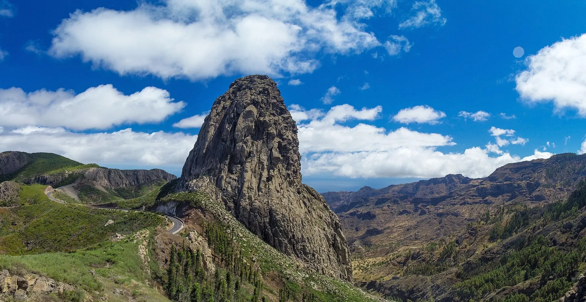 Roque de Agando, the volcanic plug at Los Roques, under a blue sky with the road winding past it.