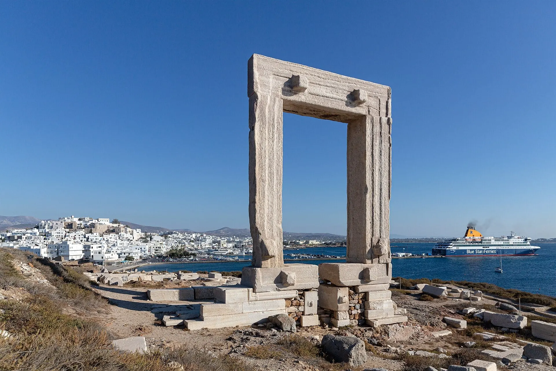 Die Portara von Naxos rahmt den weißen Ort Chora, im Hafen die Blue Star Delos.