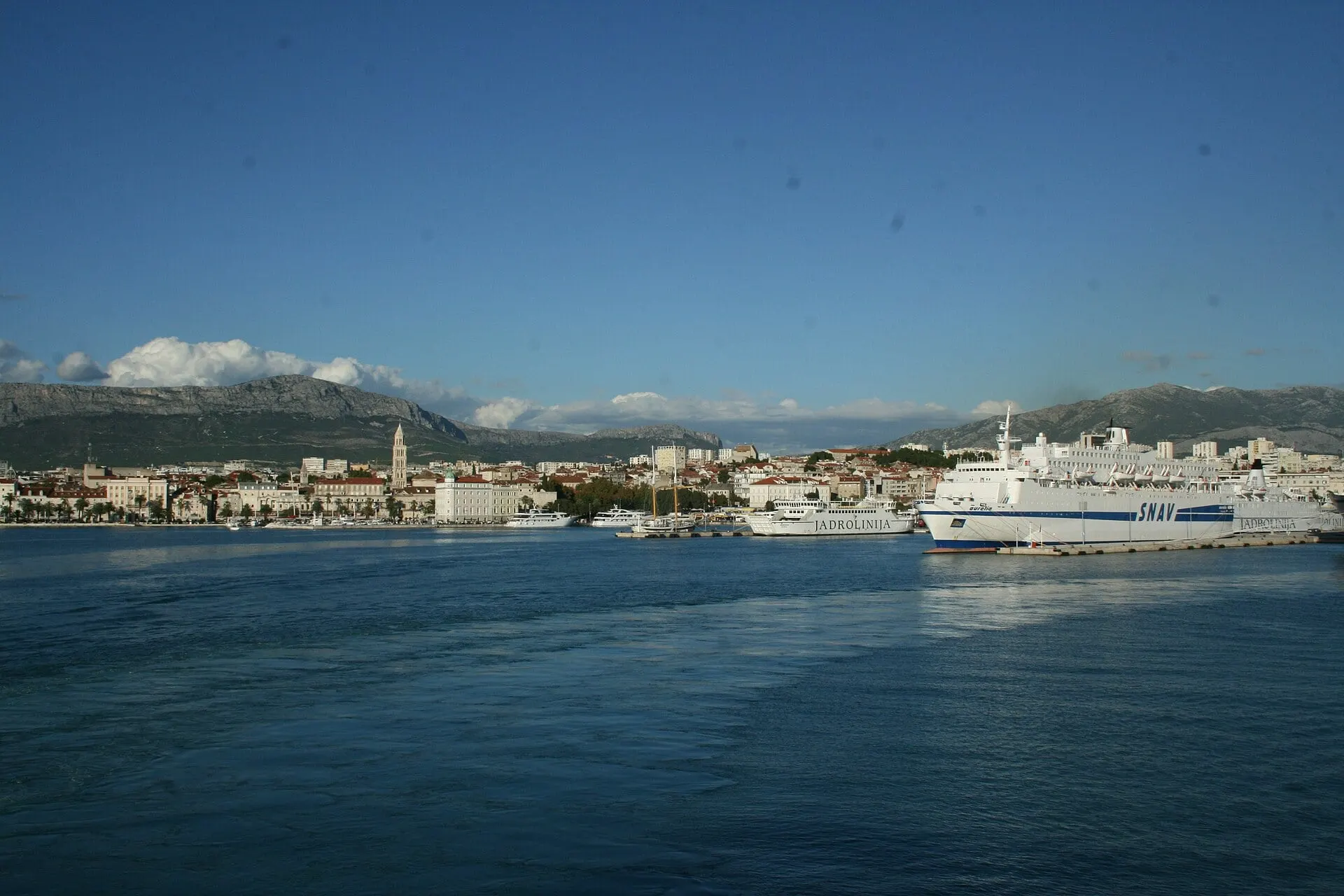 Split's harbour and waterfront from the water, with the cathedral bell tower and the mountains behind.