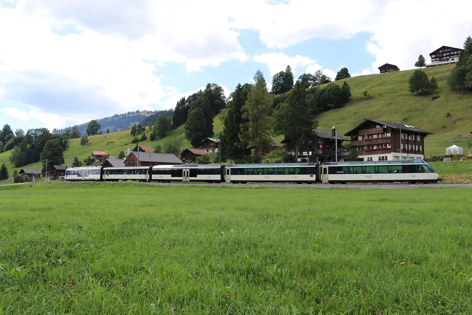 An MOB train crosses the meadows at Saanenmöser, the highest point of the line, with chalets on the slope behind.
