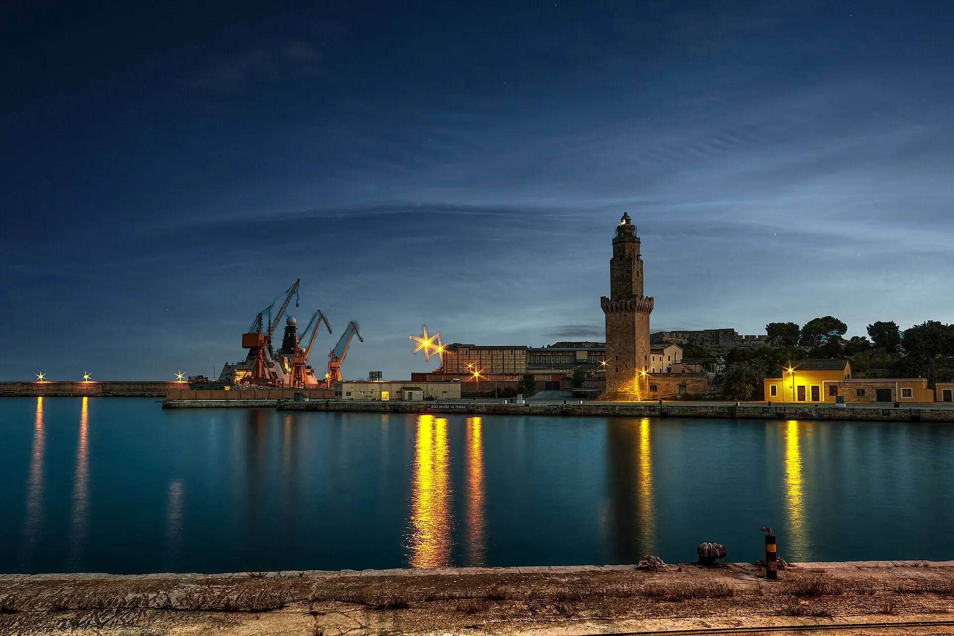 Portopí lighthouse at the harbour mouth in Palma at dusk, its lights reflected in the still water.