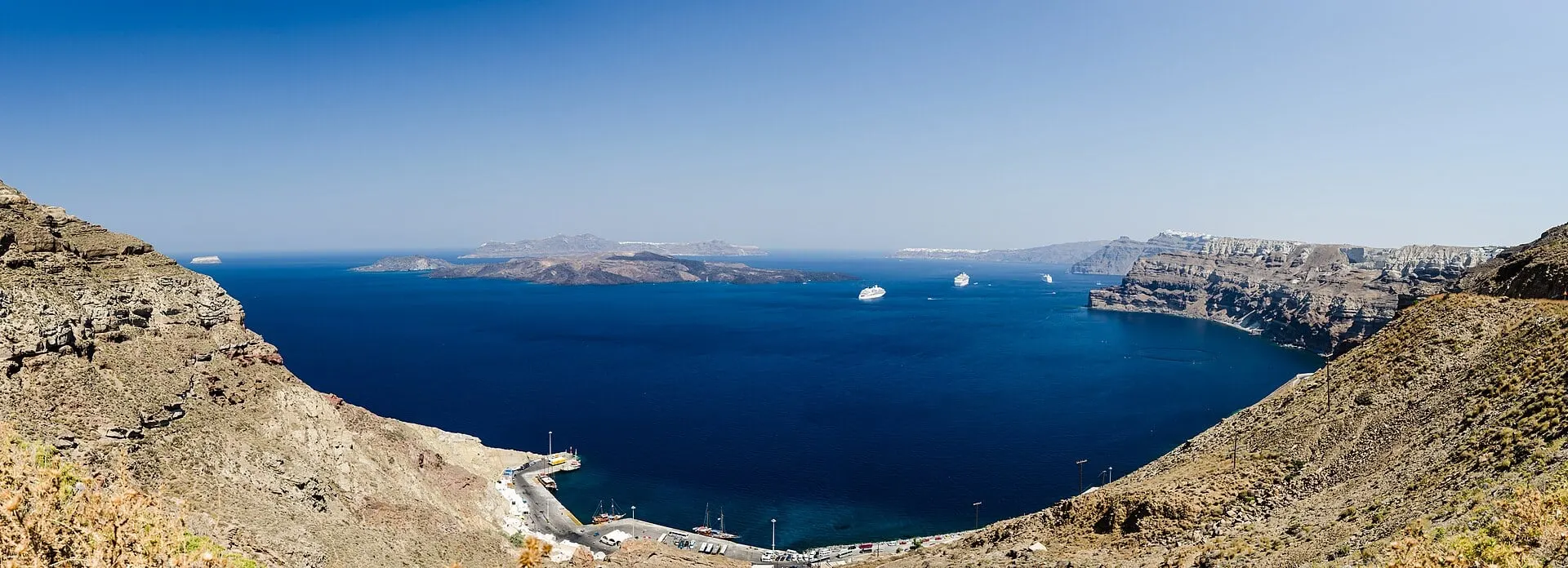 Der Hafen Athinios am Fuß der Klippen, dahinter die Caldera von Santorini und die Kameni-Inseln.