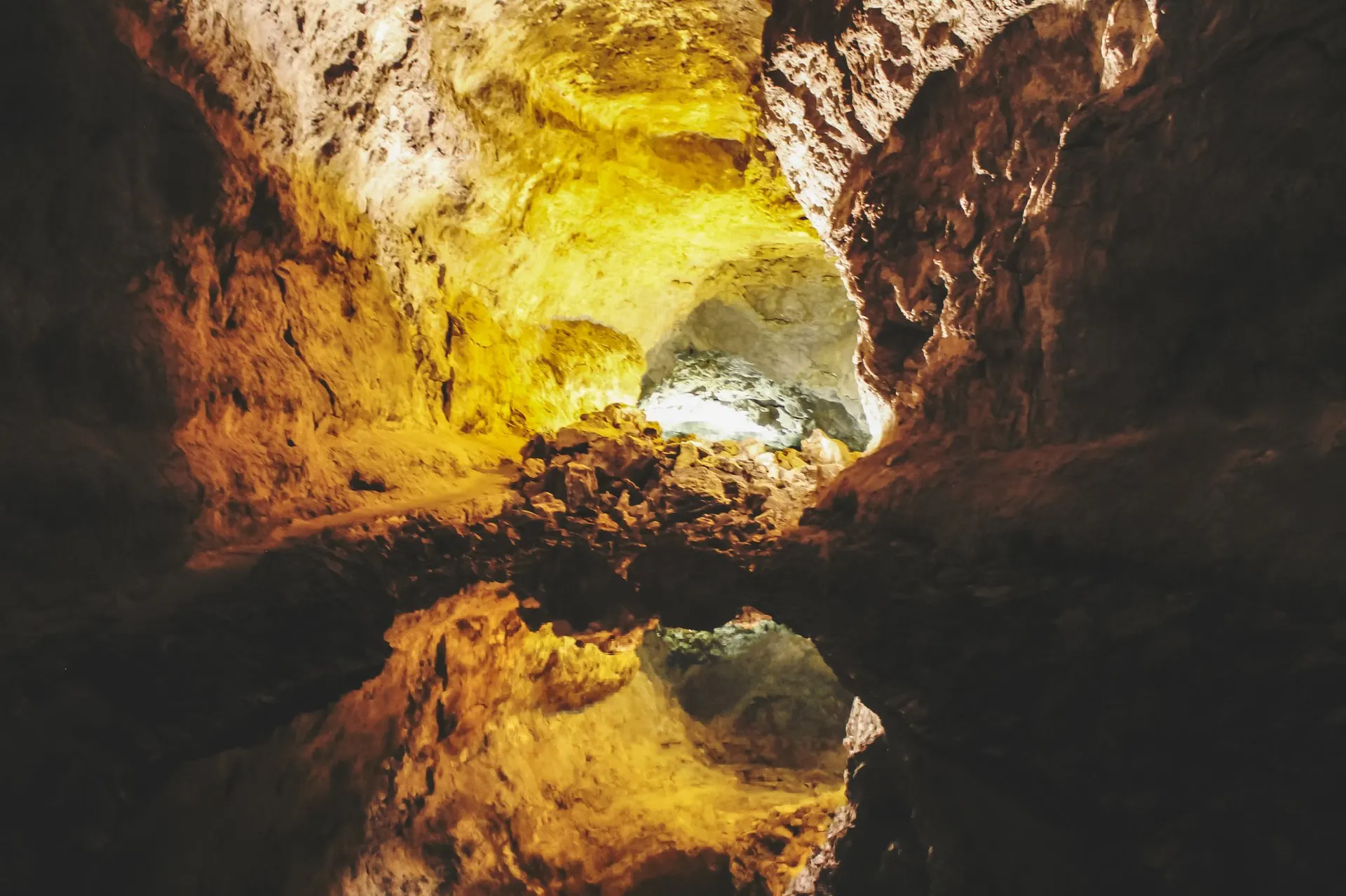 Lit rock walls inside Cueva de los Verdes, reflected in still water on the cave floor