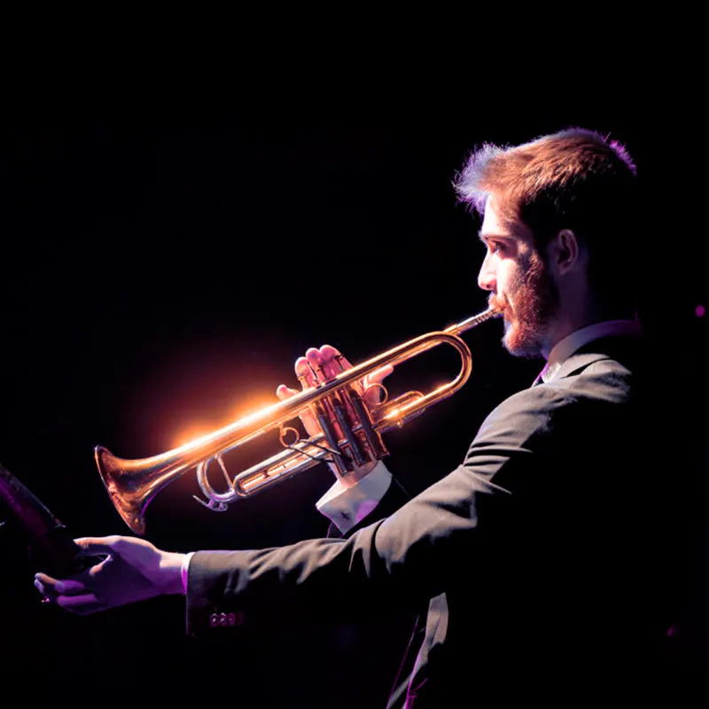 The Jazz Roomで、ダークスーツのトランペット奏者がスポットライトの中でソロを吹いている