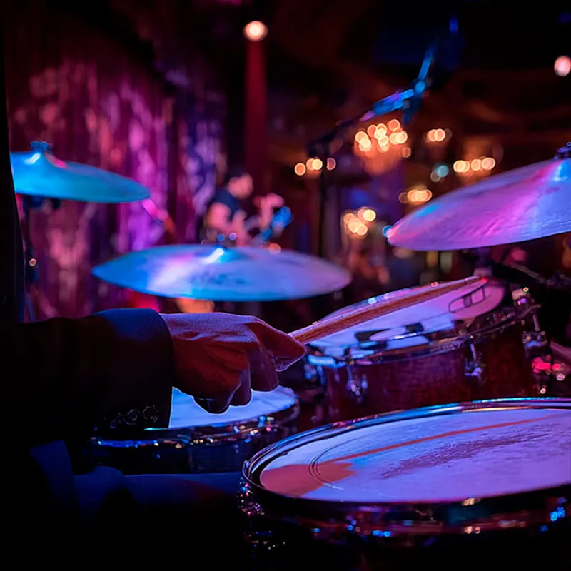 The Jazz Roomで、紫と赤の舞台照明の下でドラマーが演奏している