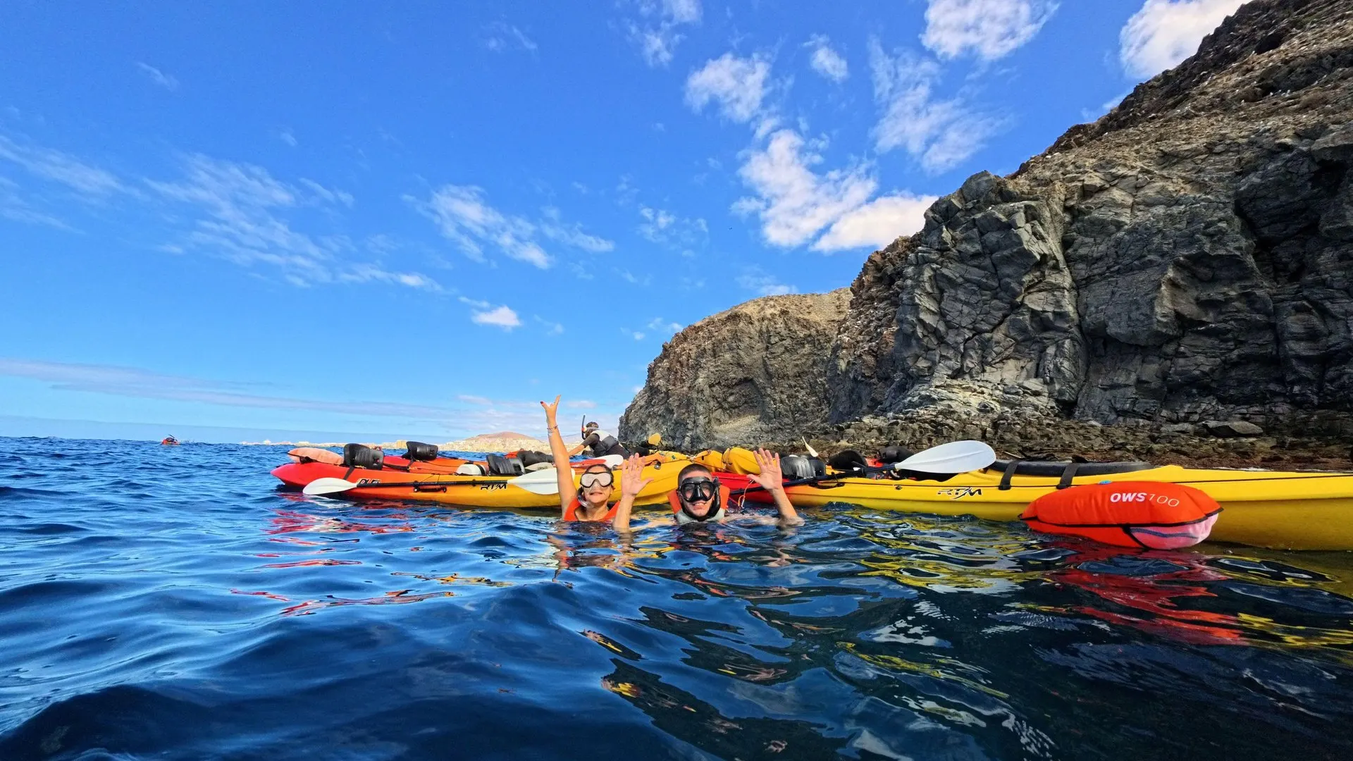Kayaks rafted together under a dark volcanic cliff