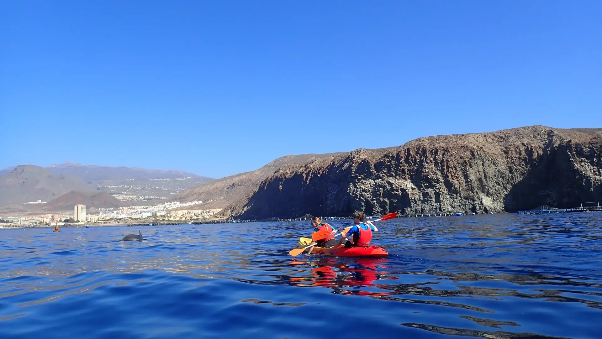 Two kayakers paddling below a line of coastal cliffs