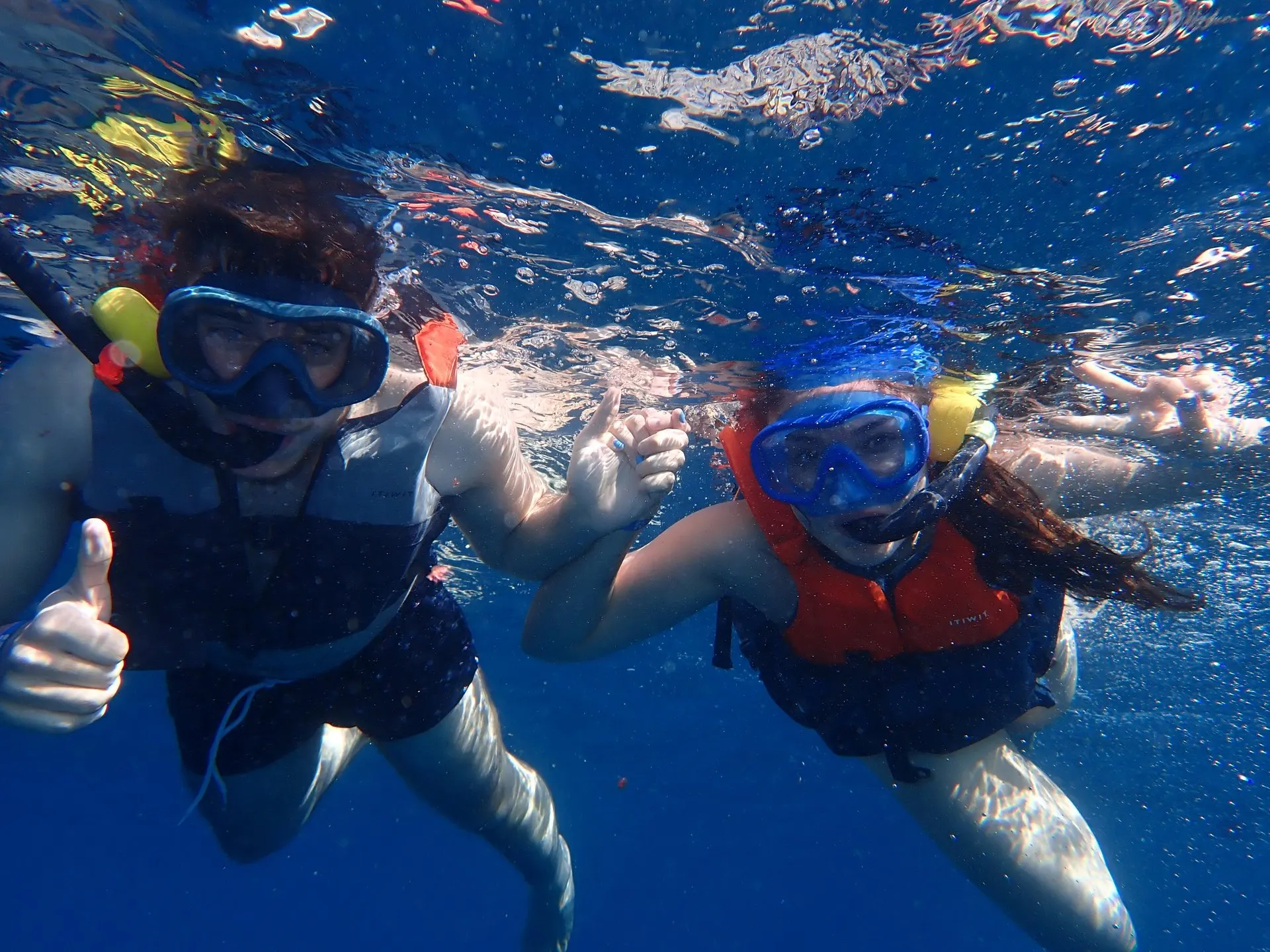 Two snorkellers in masks giving a thumbs up under water