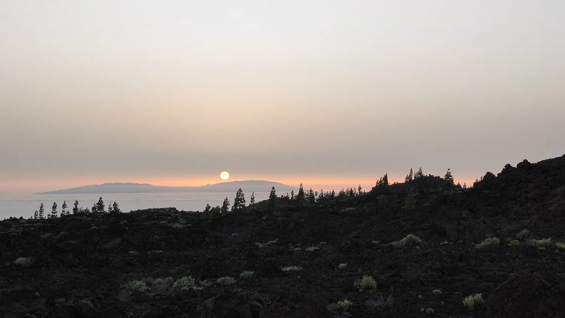 Il sole che tramonta dietro La Gomera sopra un mare di nuvole, visto dai campi di lava occidentali del Teide