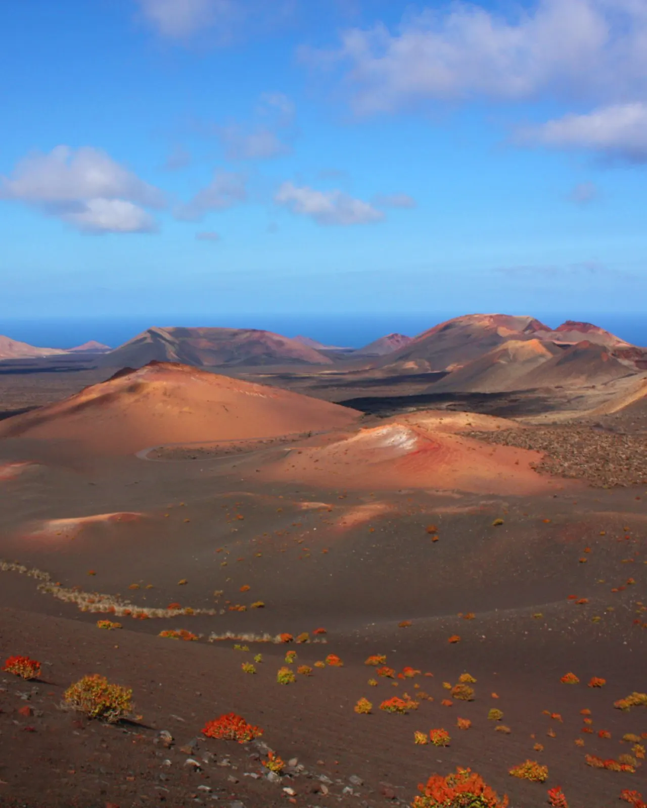 Red and ochre volcanic cones in Timanfaya National Park, with the sea beyond