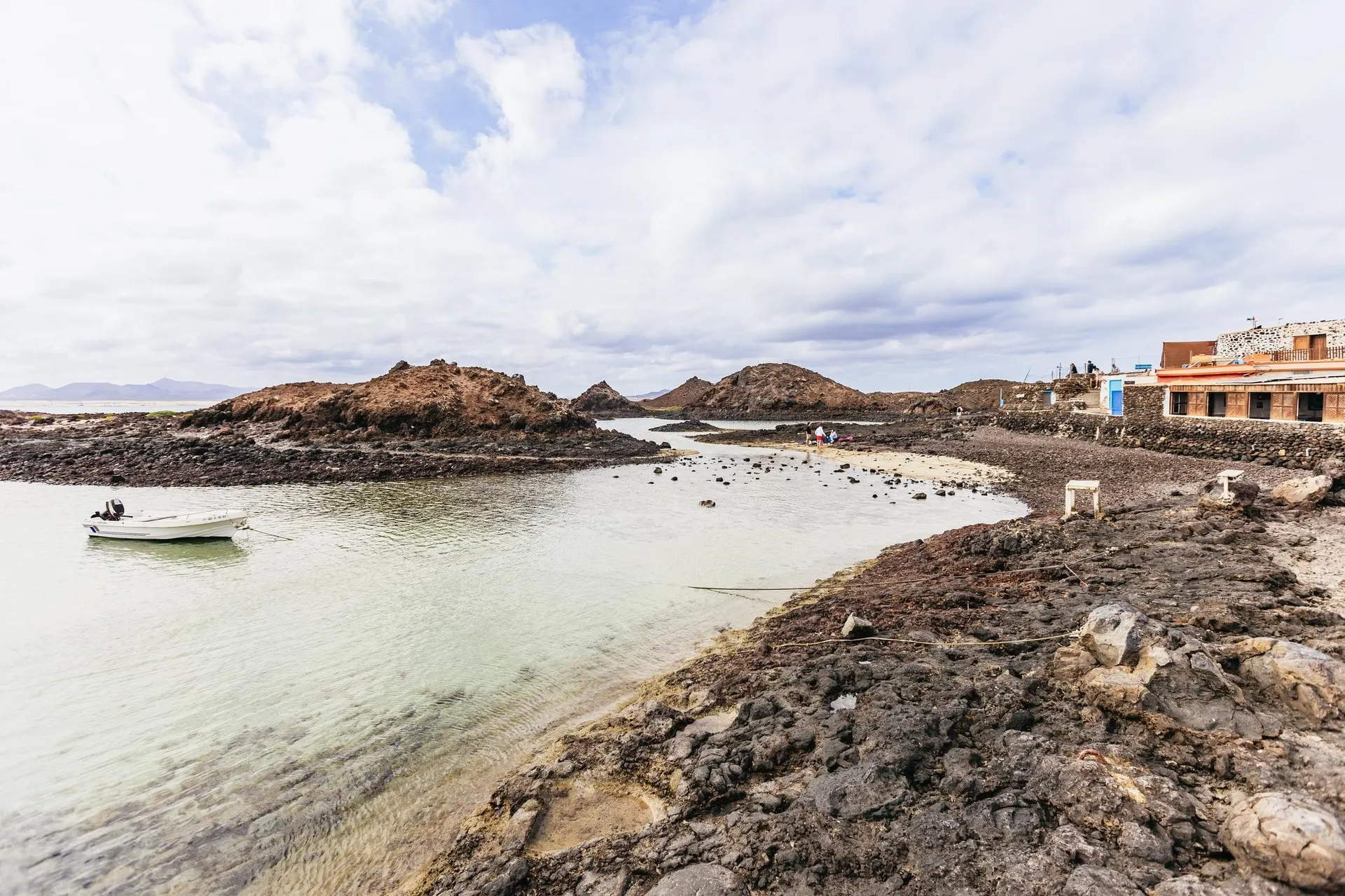 The shallow lagoon and lava shore of El Puertito on Isla de Lobos, with a small boat moored and the old fishermen's houses on the right