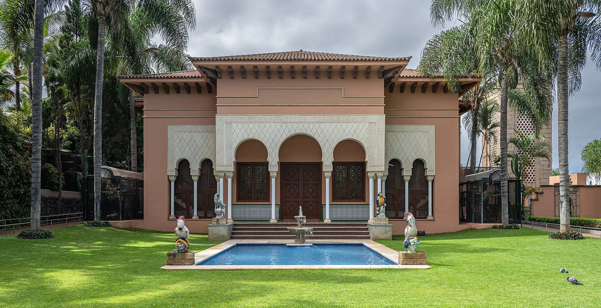 A Moorish-style pavilion with parrot statues, a fountain and lawns among palm trees at Loro Parque