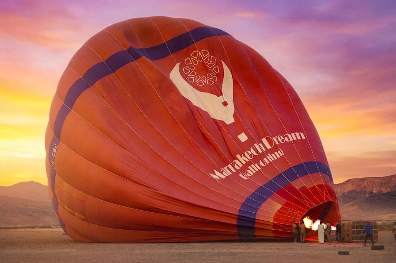 Crew filling a Marrakech Dream Ballooning balloon with hot air from the burner as it lies on the ground before dawn, hills behind