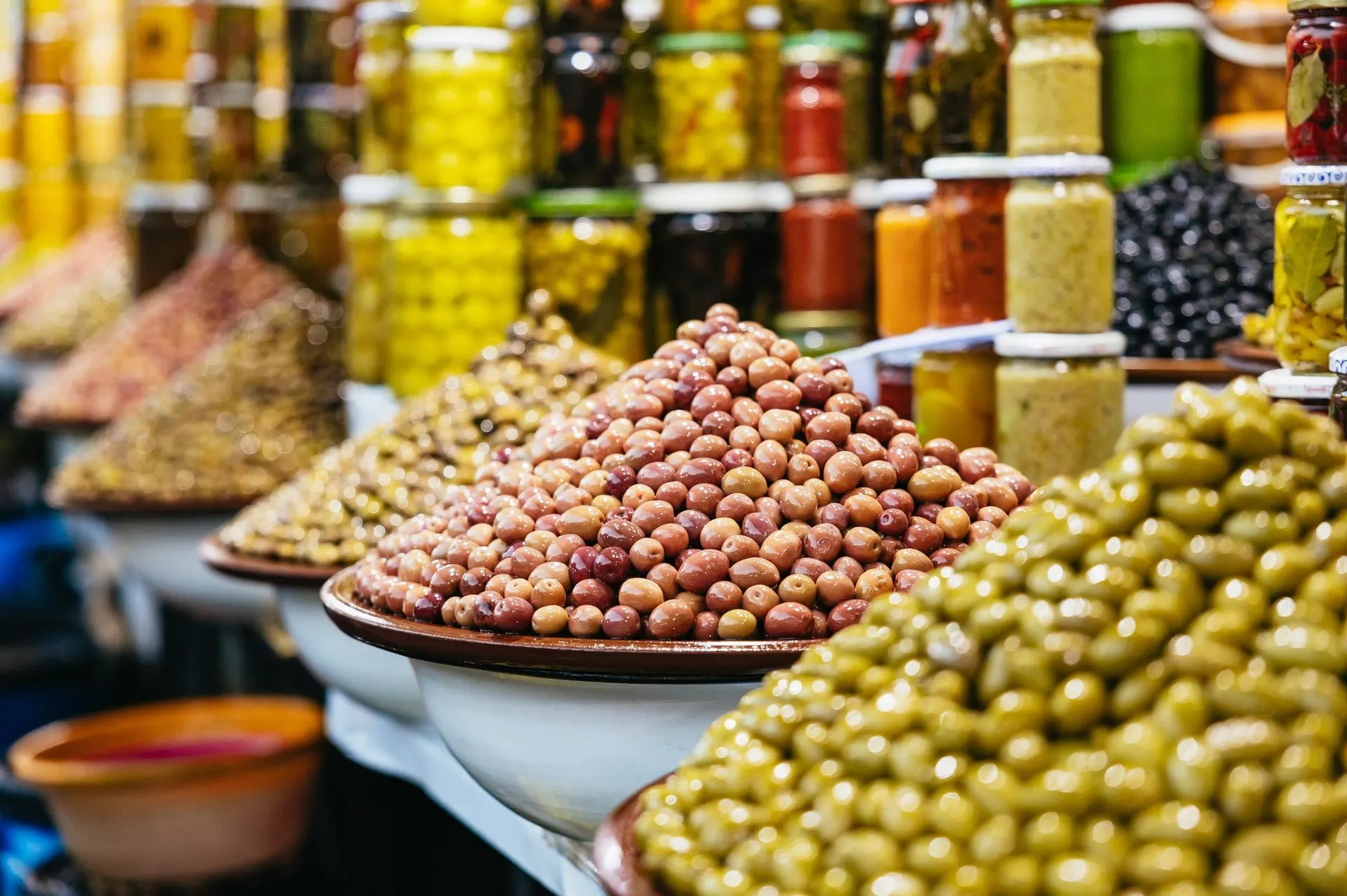 Pyramids of green and red olives in bowls at a Medina market stall, with jars of preserved lemons behind