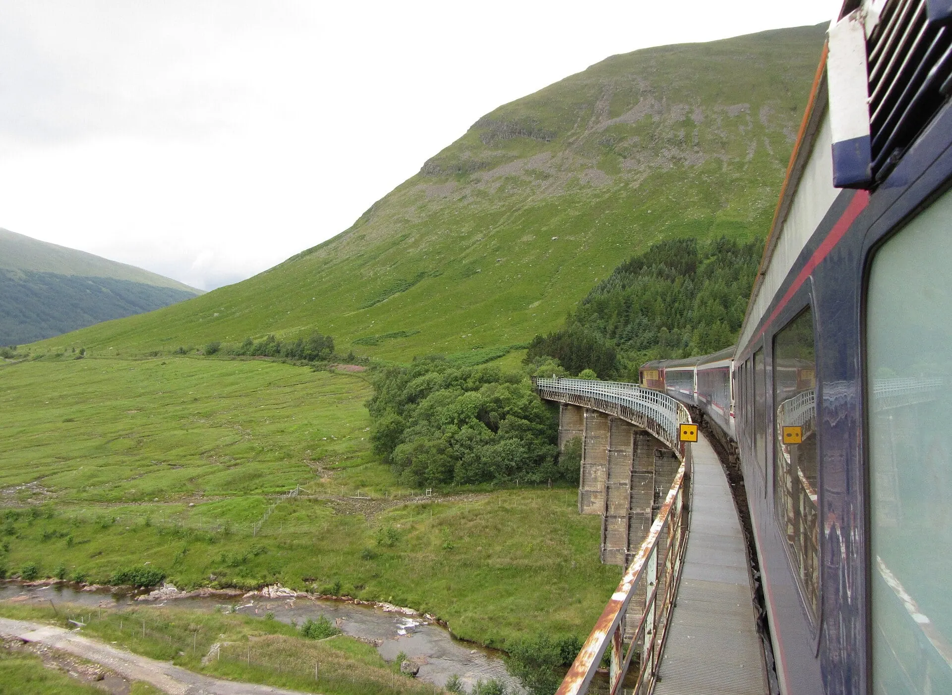 The view from a train window as it rounds a viaduct on the Horseshoe Curve beneath a grassy mountainside.