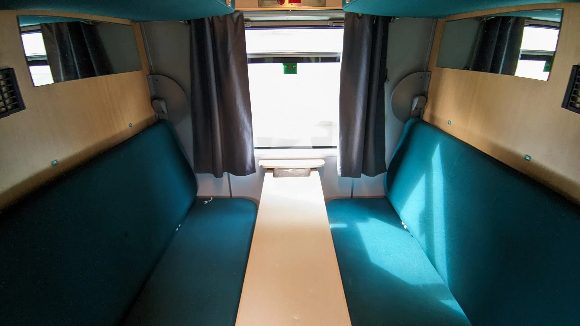 A compartment with green seats and a fold out table in a Vy night train couchette car used on the Bergen Line.