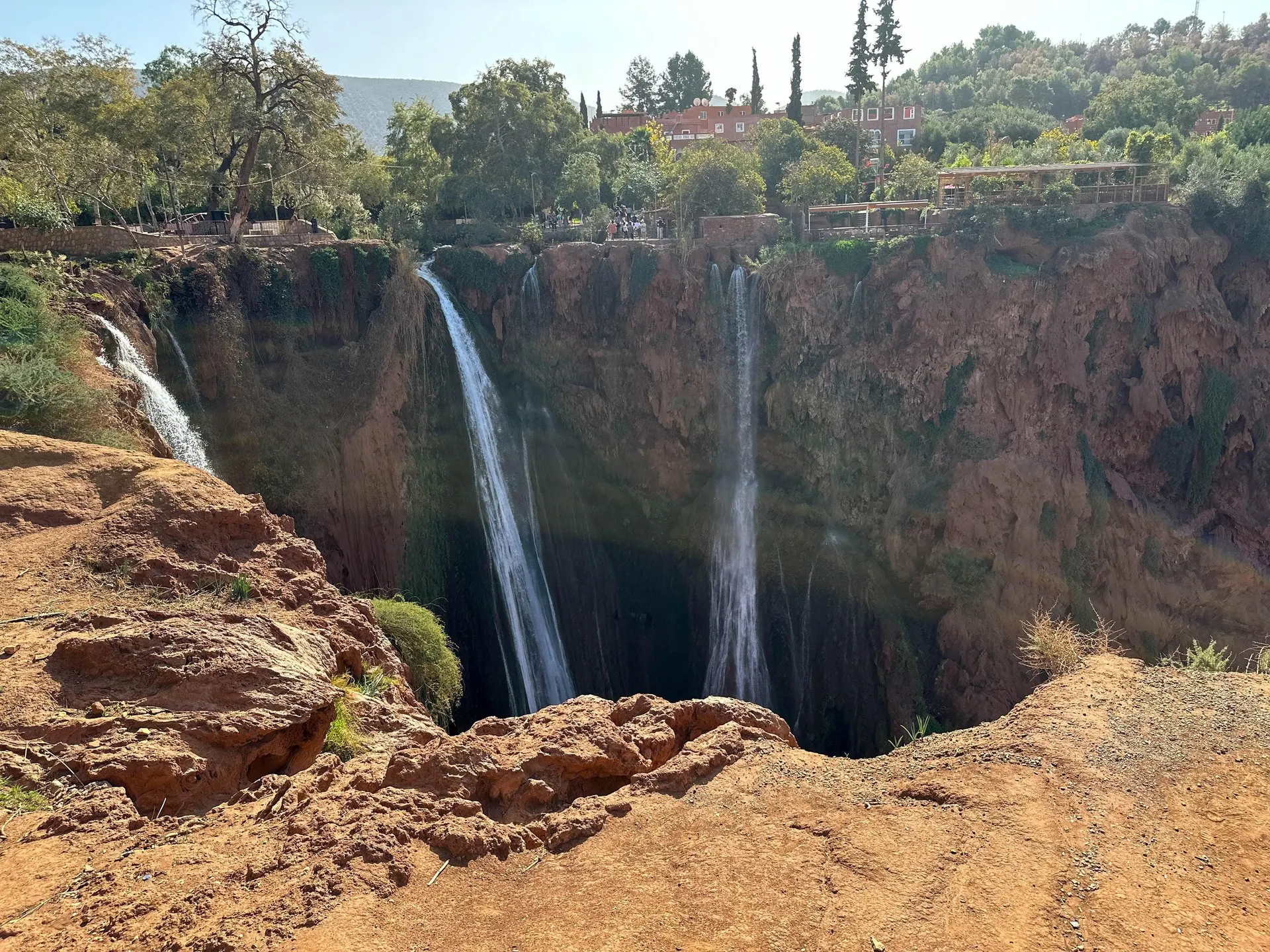 The Ouzoud falls dropping into the red gorge, seen from the rocky rim, with visitors on the terraces opposite