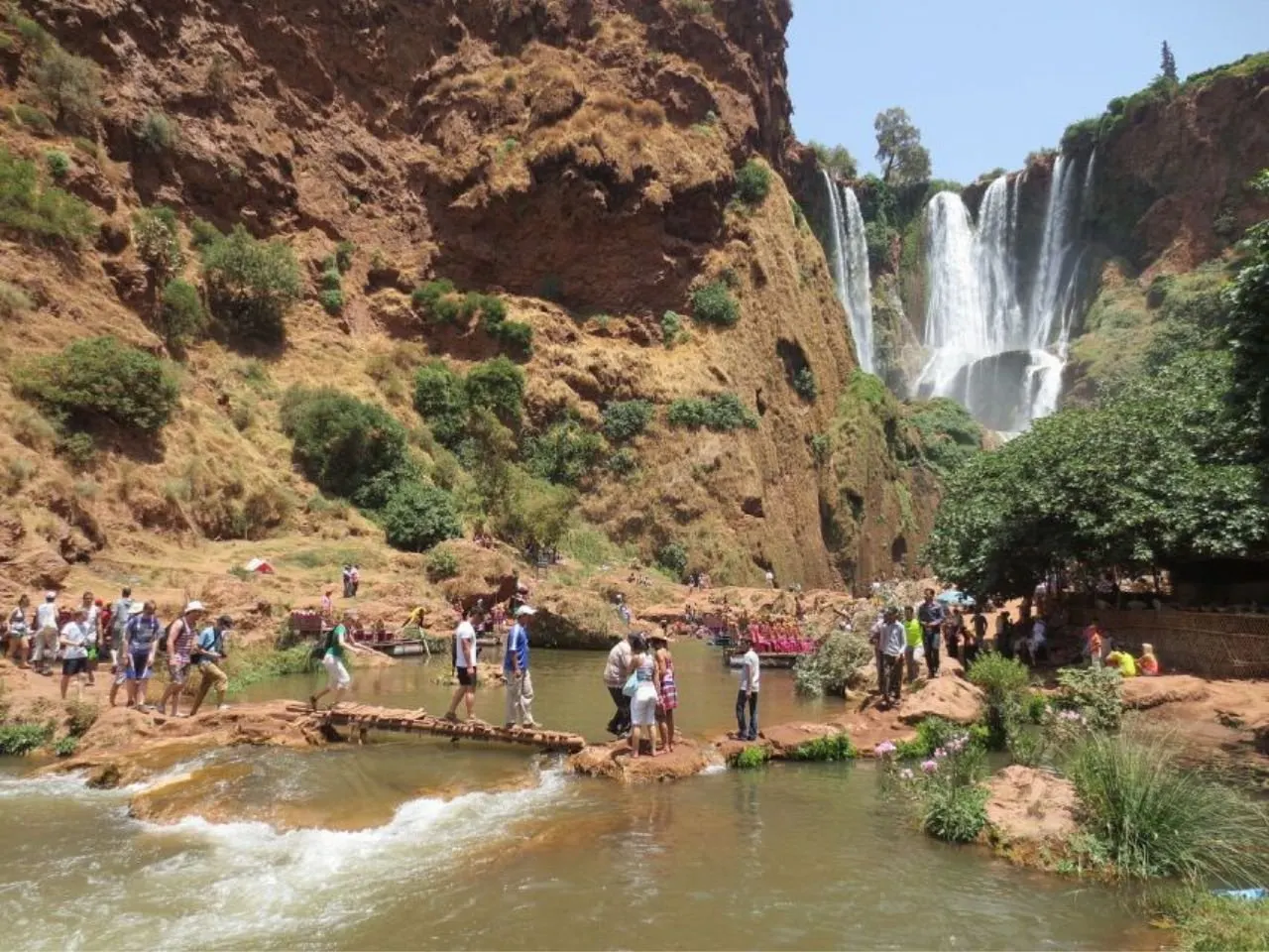 Visitors crossing a plank bridge over the river at the bottom of the gorge, with the falls behind