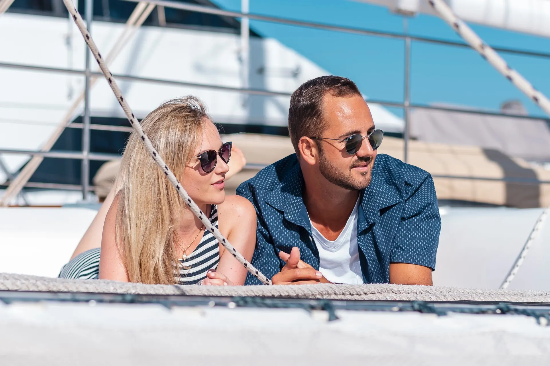 A couple lying on the front nets of the catamaran, looking out to sea