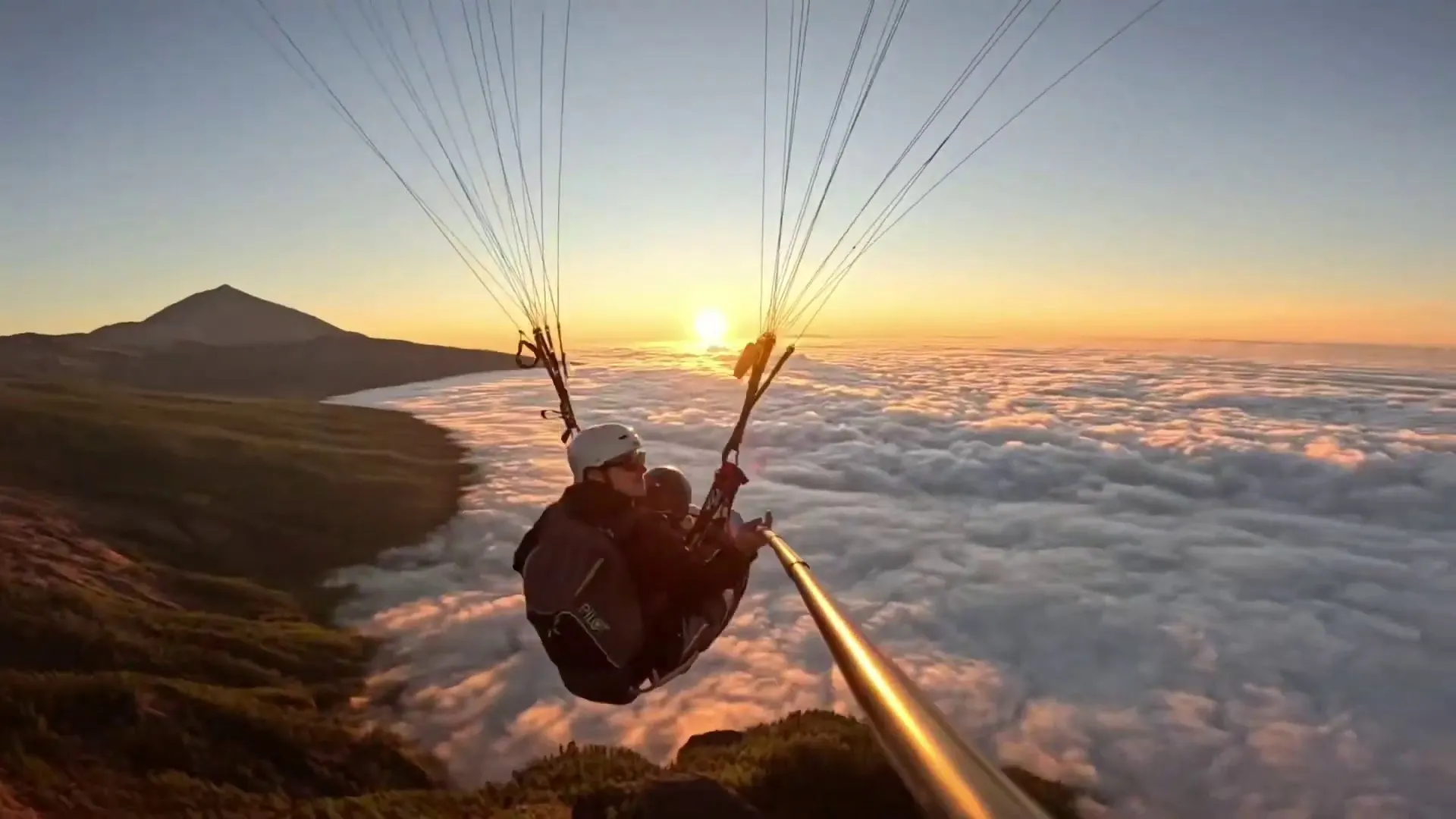 A tandem paraglider above the sea of cloud at sunset, with Teide on the horizon