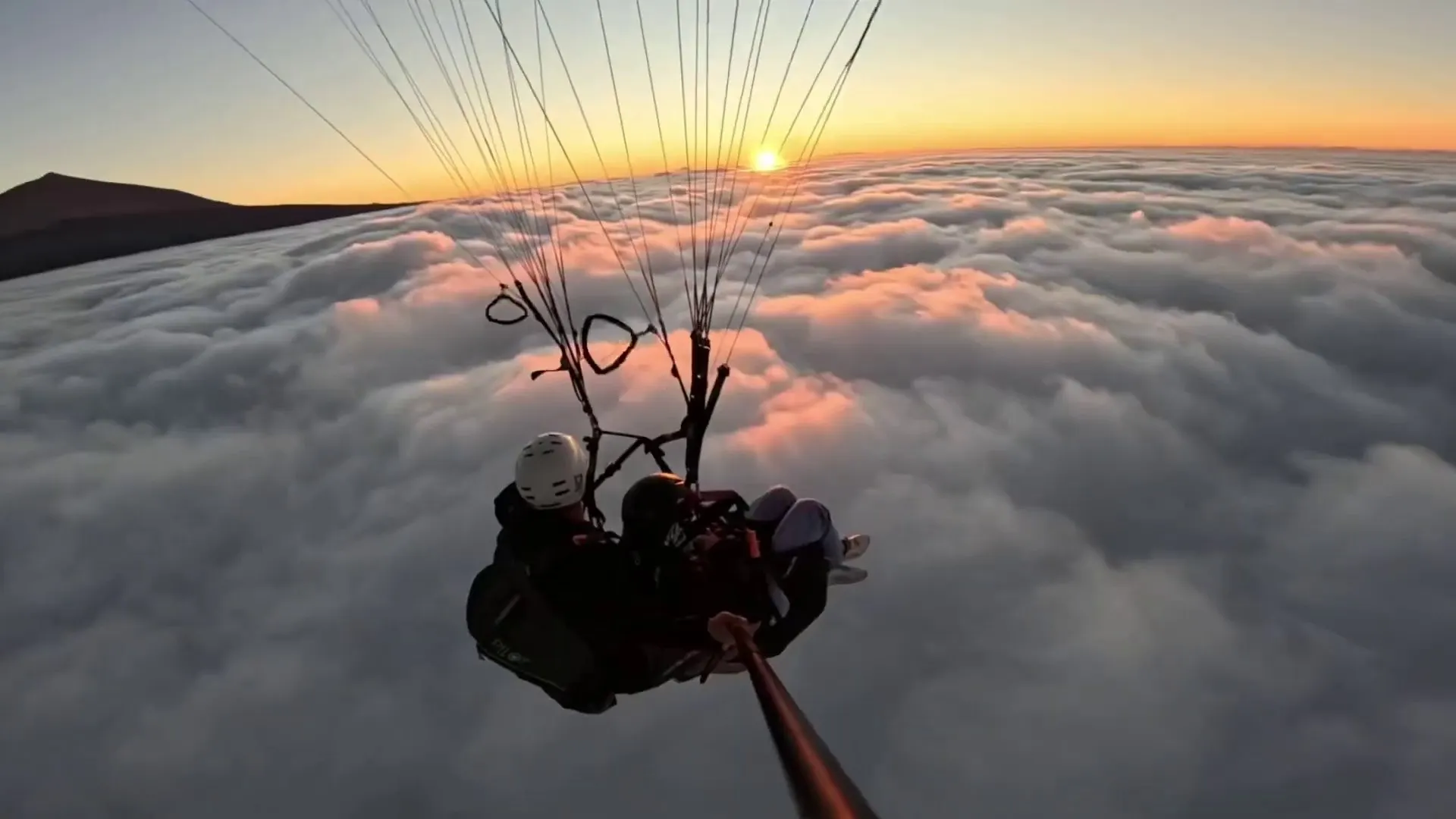 A tandem pair flying over a sea of cloud as the sun sets