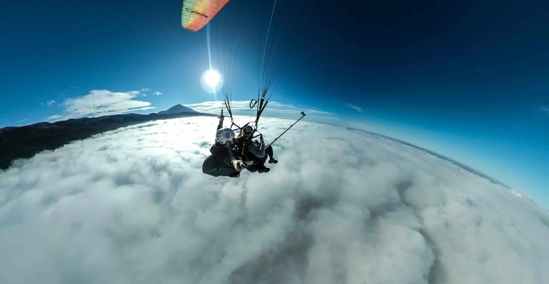 A tandem paraglider high above the clouds in bright sun