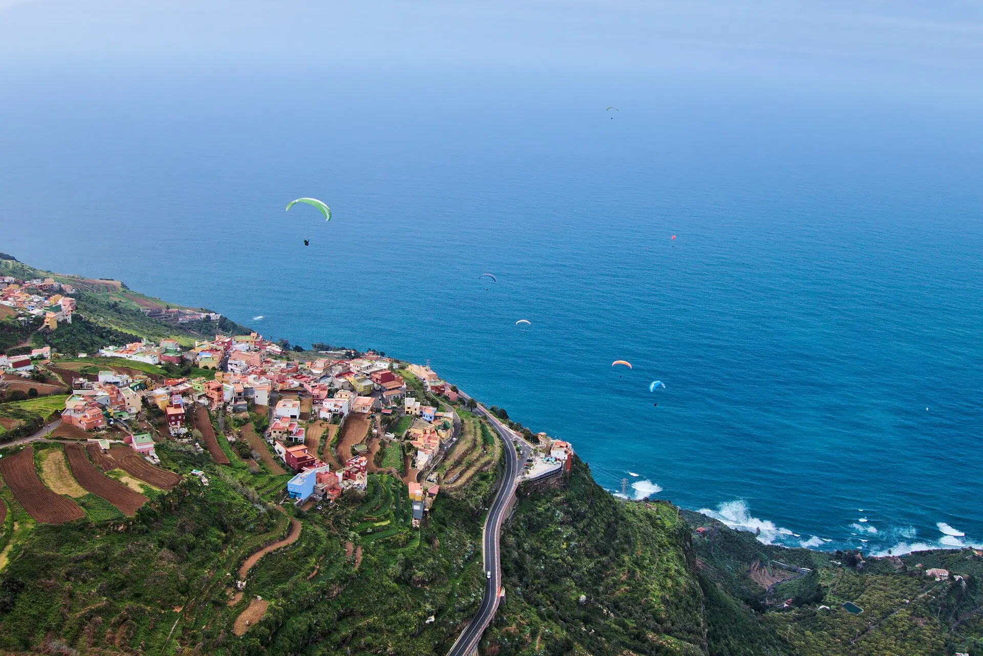 Paragliders over the sea off Tenerife's north coast, with a clifftop village and a coast road below