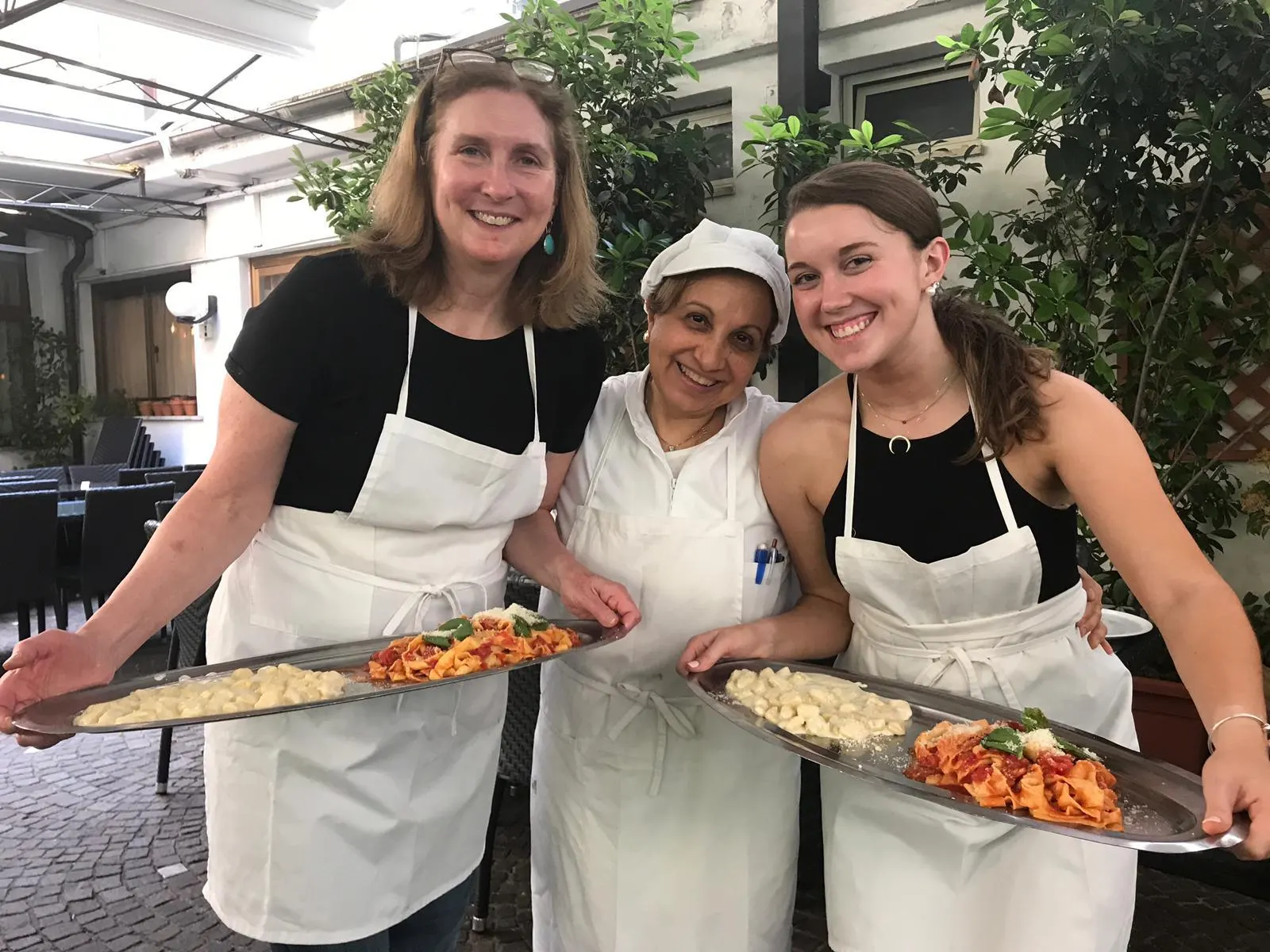 A chef and two guests with trays of pasta they made
