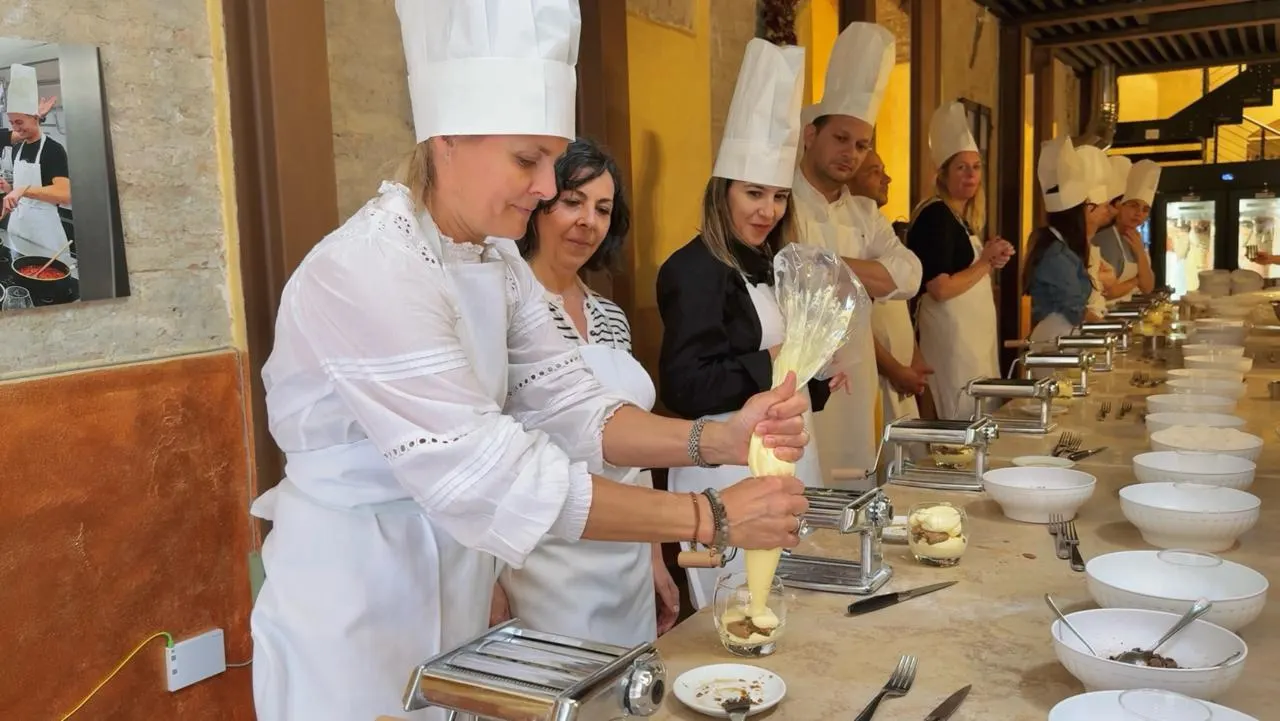 Guests in chef's hats making tiramisù at a long table