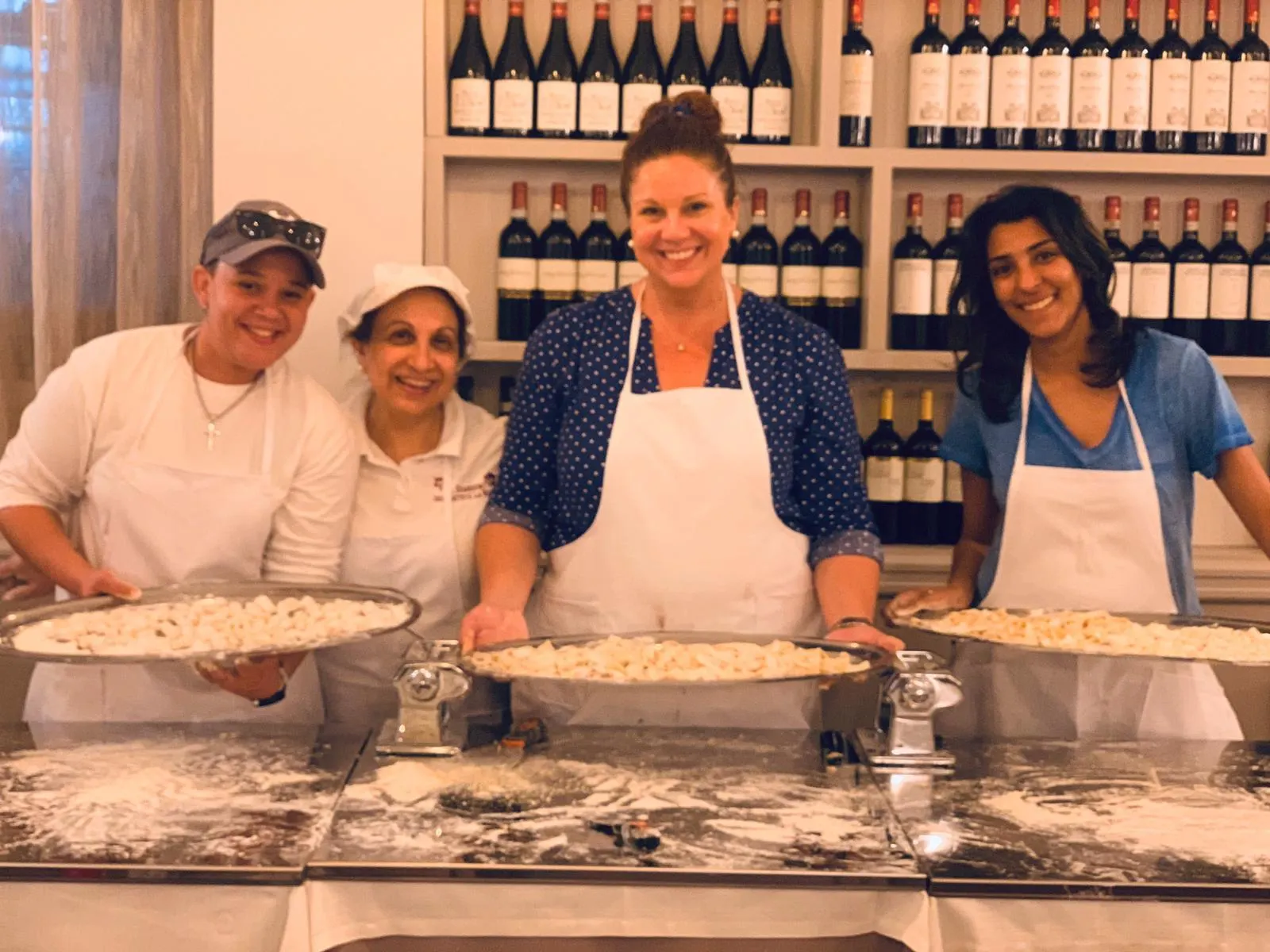 Guests and chefs with the pasta they made, in front of a wine wall