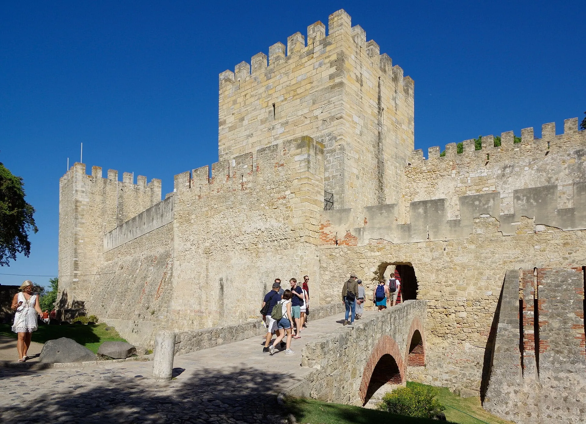 Visitors crossing the bridge to the walls and keep of São Jorge Castle under a blue sky