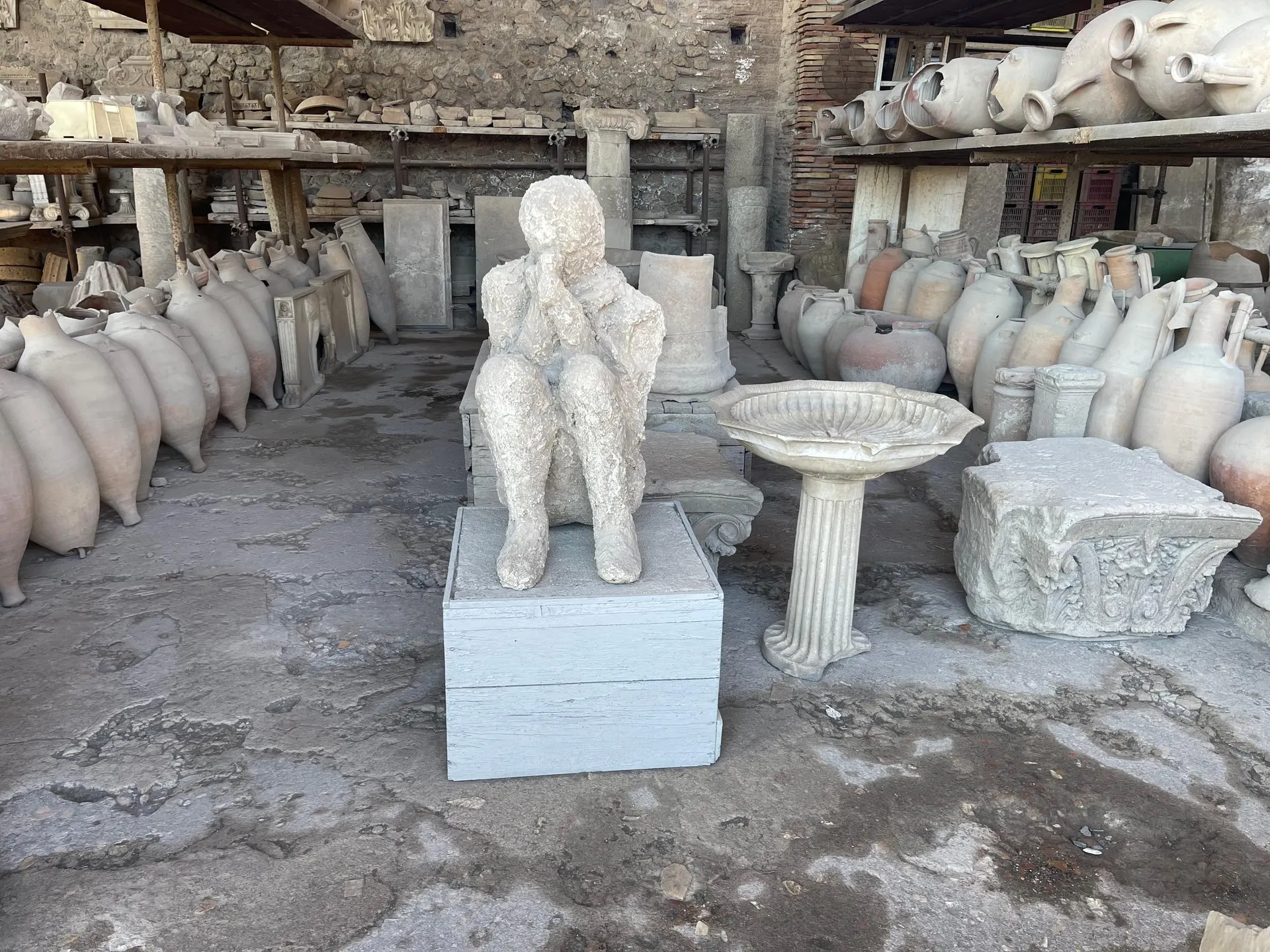 The plaster cast of a seated victim of the eruption among amphorae and stone fragments in the Granary of the Forum at Pompeii