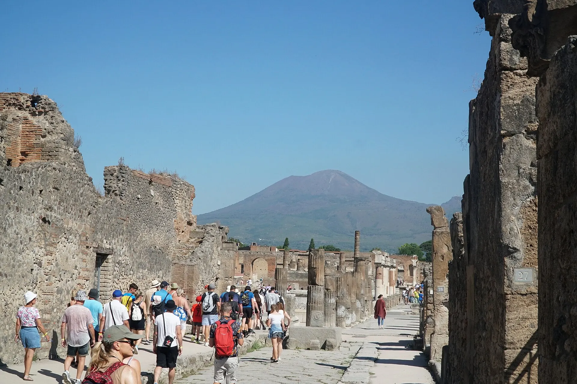 Visitors walking a paved Roman street towards the Forum of Pompeii, with Vesuvius behind