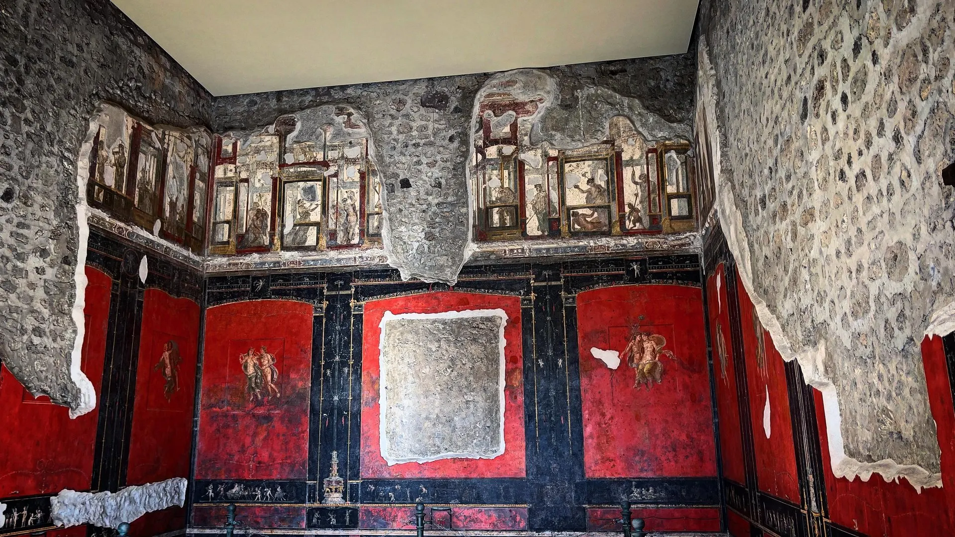 A room in Pompeii with red and black painted wall panels and fragments of frescoed figures above