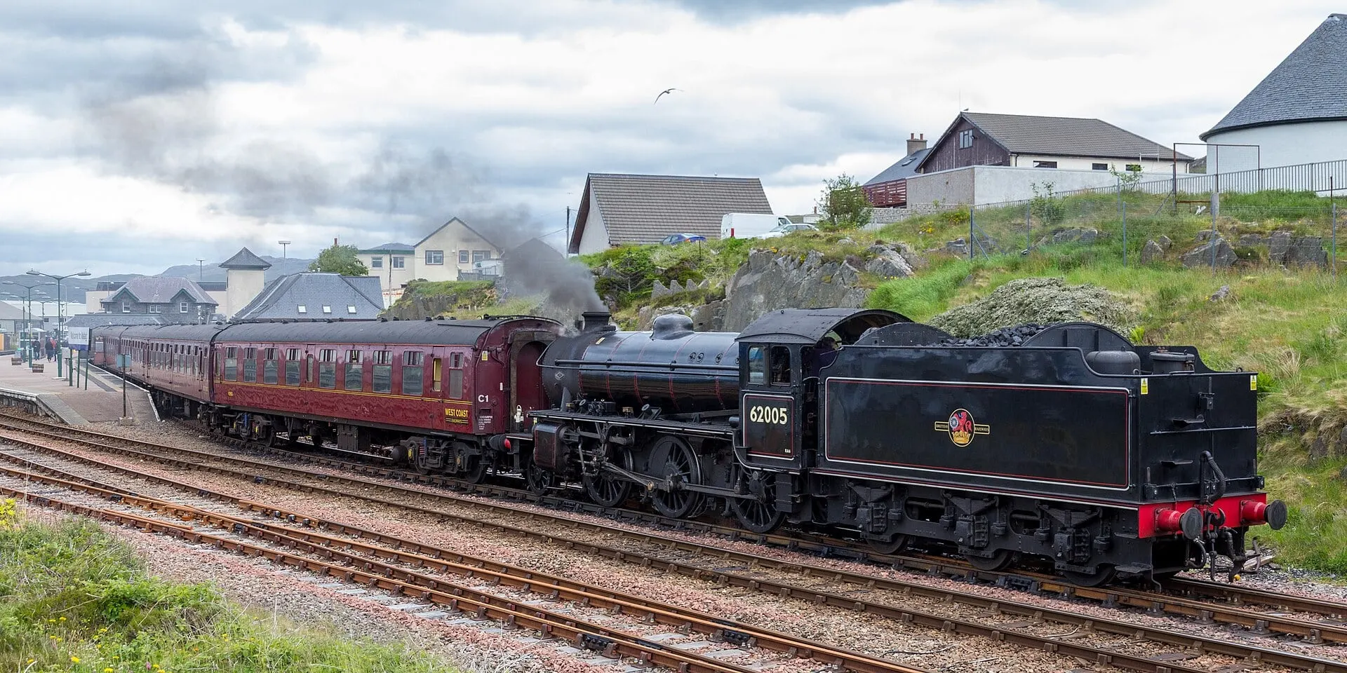 The Jacobite steam locomotive and its maroon carriages beside the platform at Mallaig station.