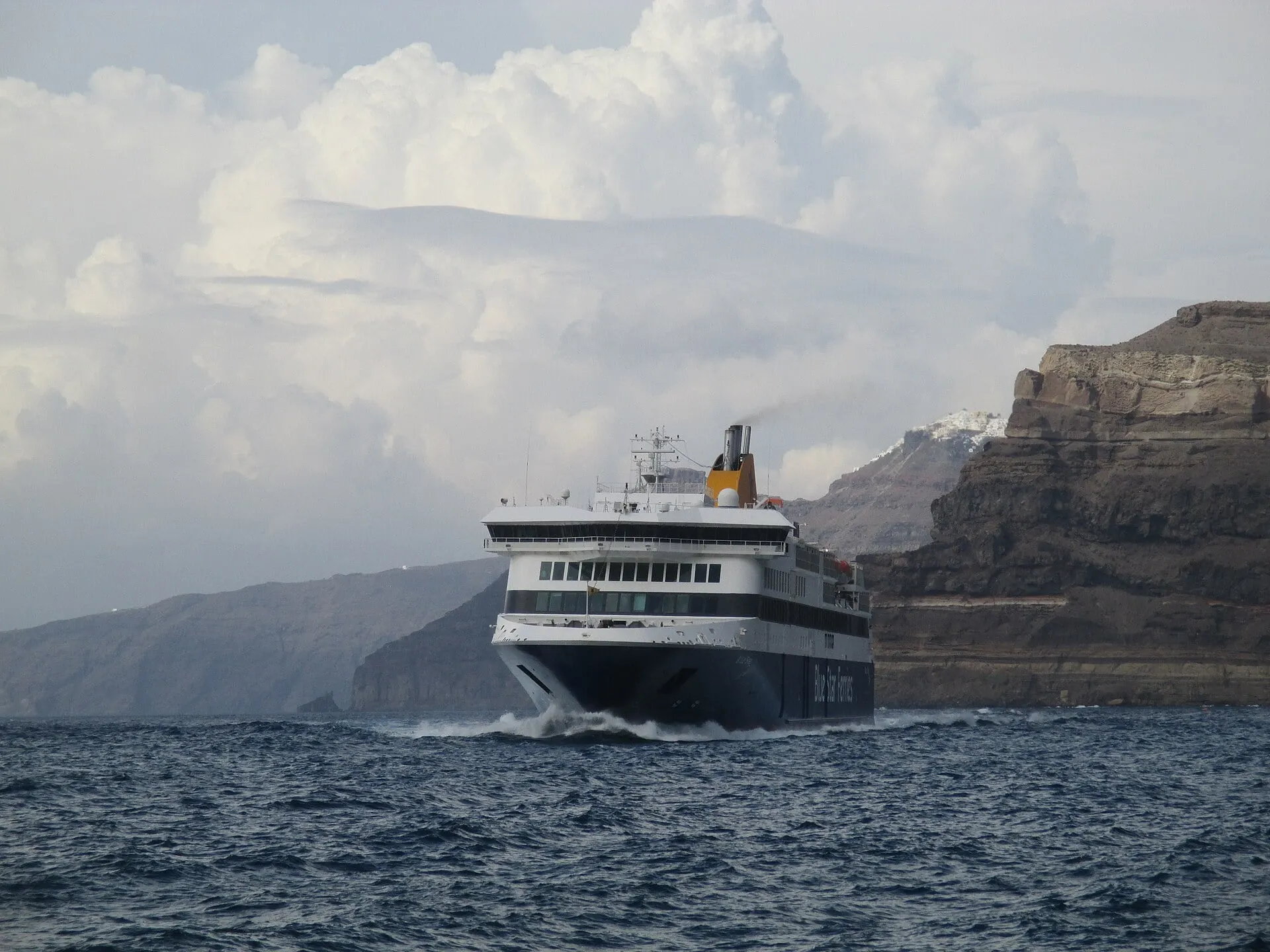 Die Blue Star Delos fährt durch die Caldera von Santorini Richtung Athinios, unter den dunklen Vulkanklippen.